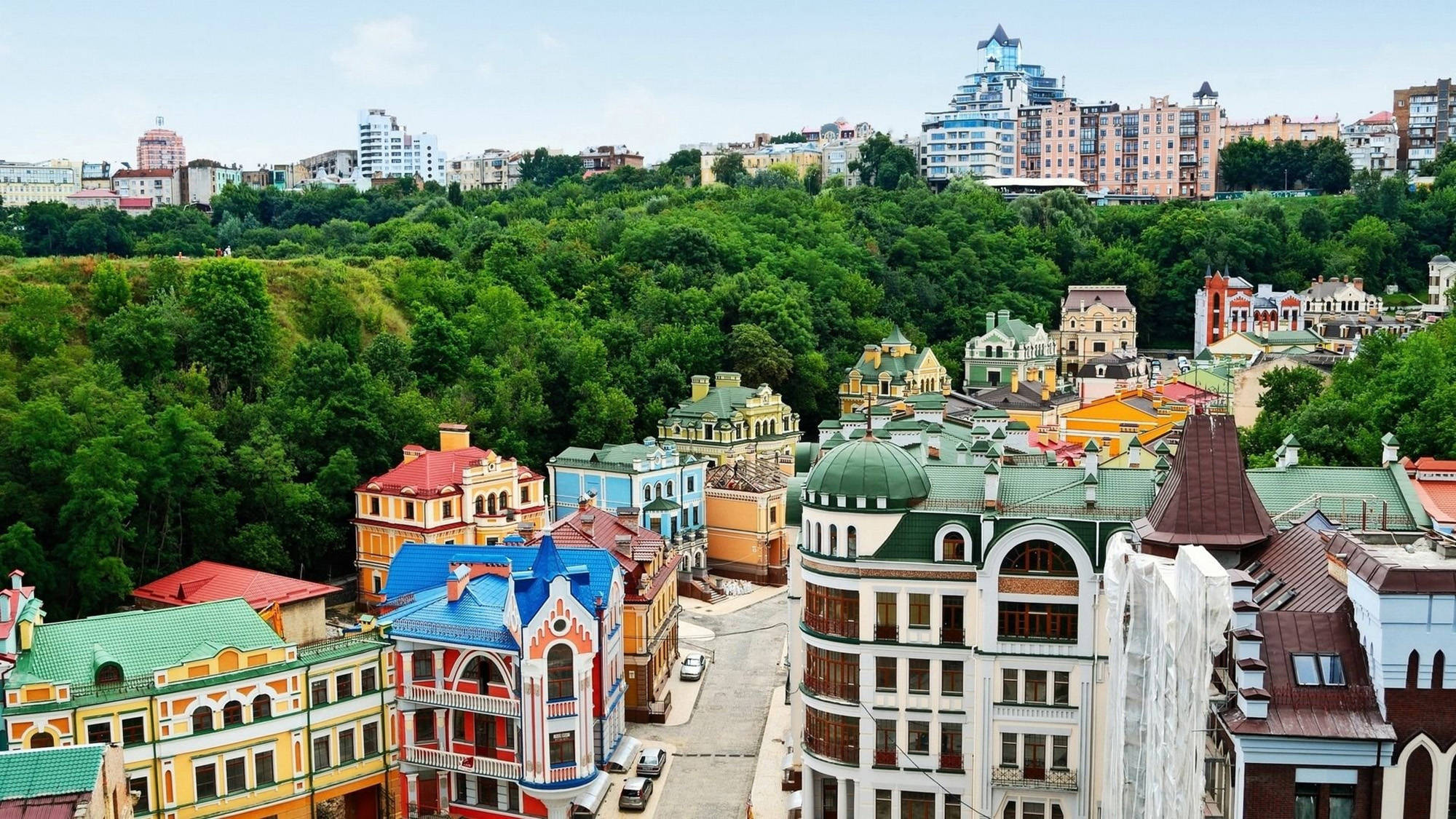 Ukraine 桌布 壁紙 — 色彩繽紛的建築物，擁有華麗的屋頂，坐落在現代高樓大廈下方的翠綠山谷中。