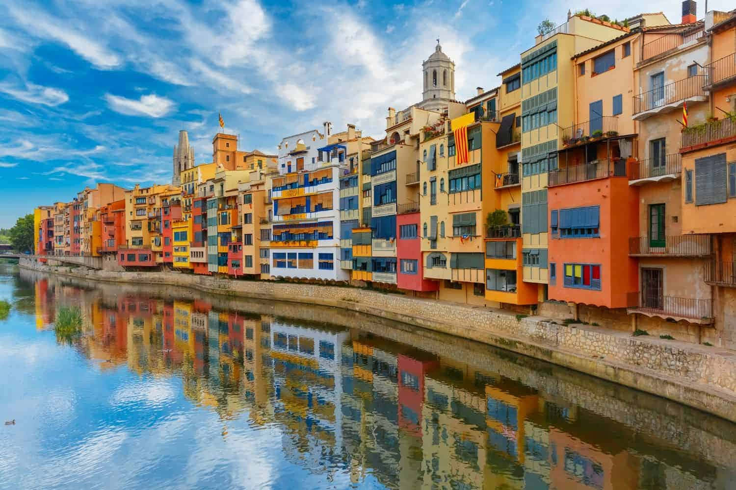 Spanish 桌布 壁紙 — 色彩繽紛的建築物沿著平靜的河流排列，上方是帶有散雲的明亮藍天。