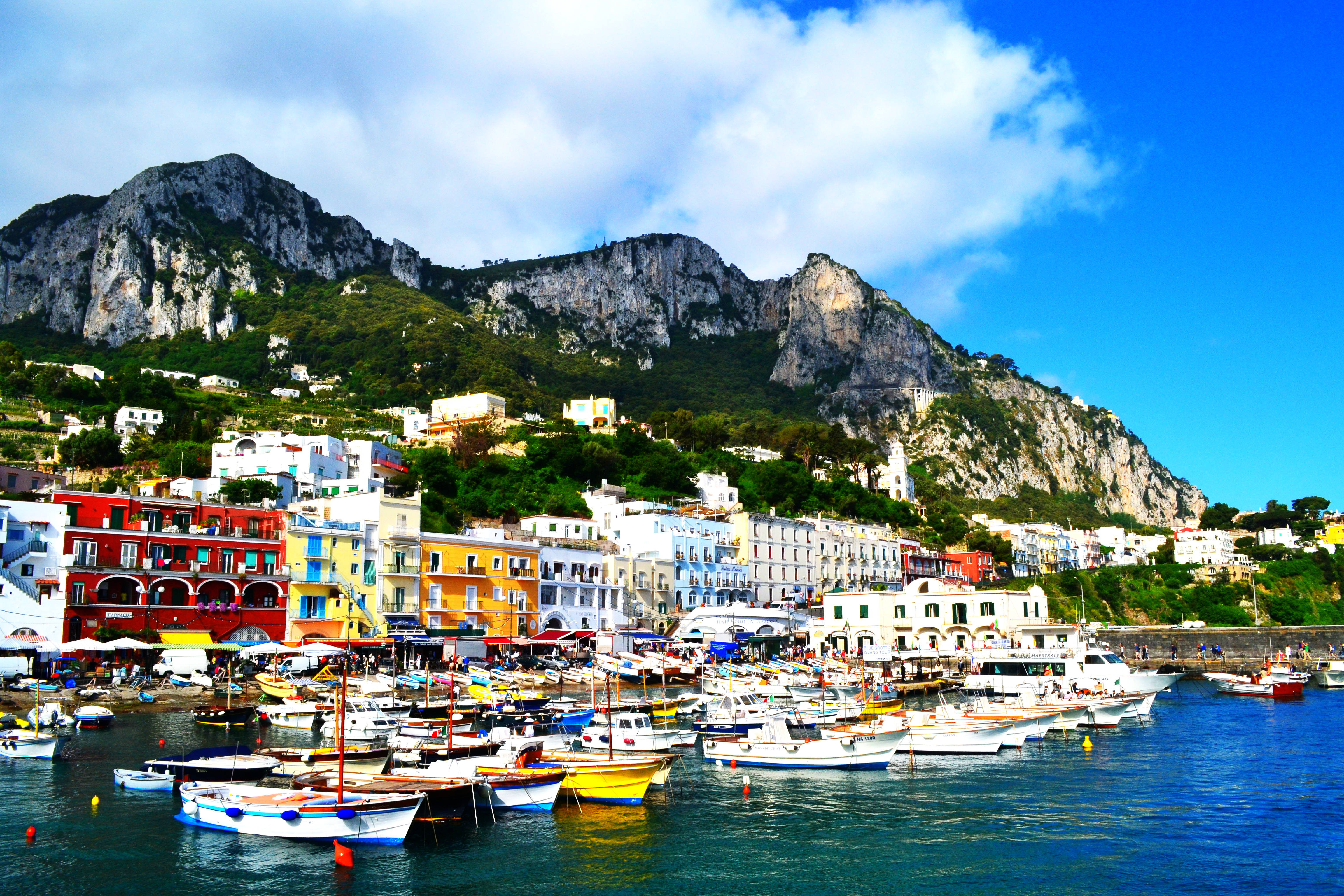 Capri 桌布 壁紙 — 色彩繽紛的建築物緊貼在陡峭的山坡上，俯瞰著繁忙的港口，港口裡停滿了船隻，天空湛藍明亮。
