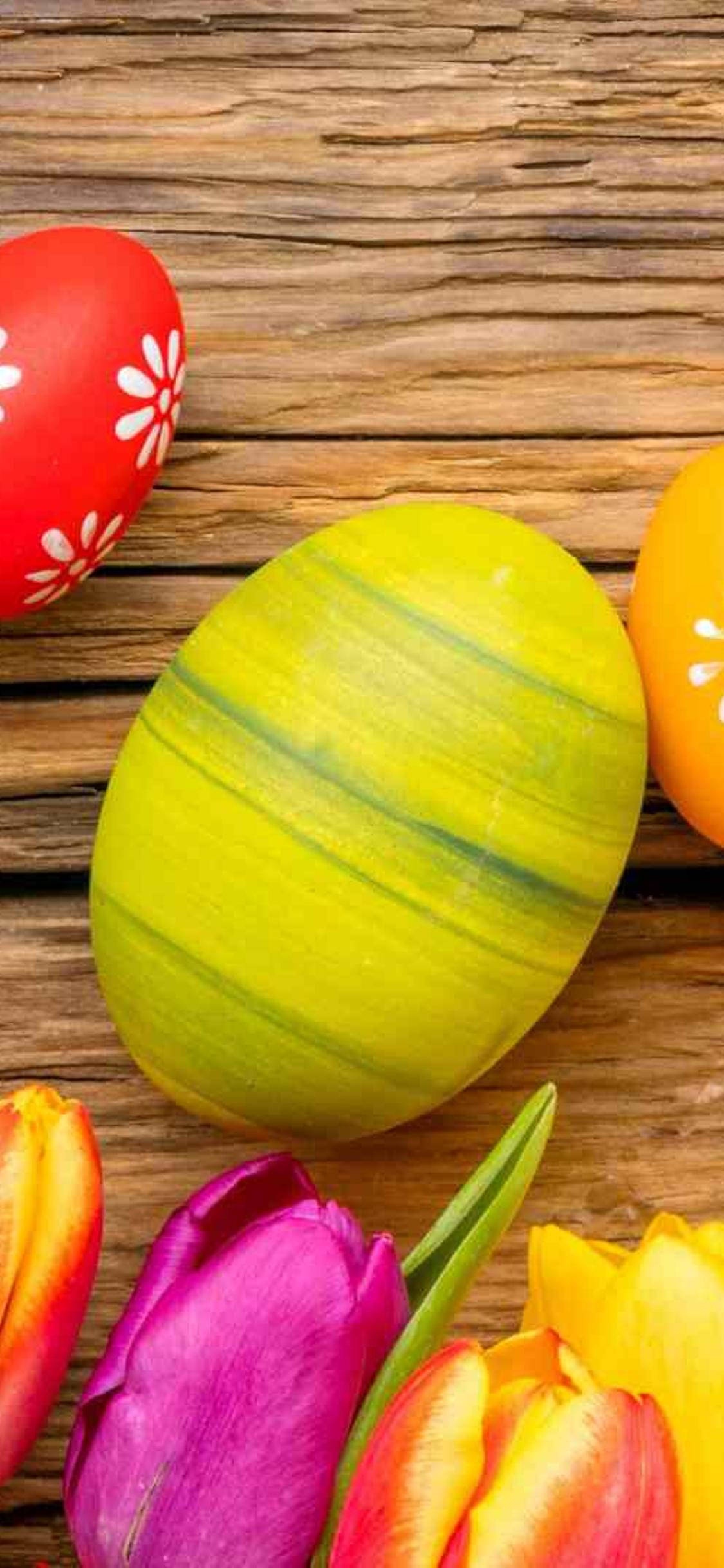 Aesthetic Easter 桌布 壁紙 — 色彩繽紛的彩繪復活節蛋和鬱金香放在質樸的木質表面上。