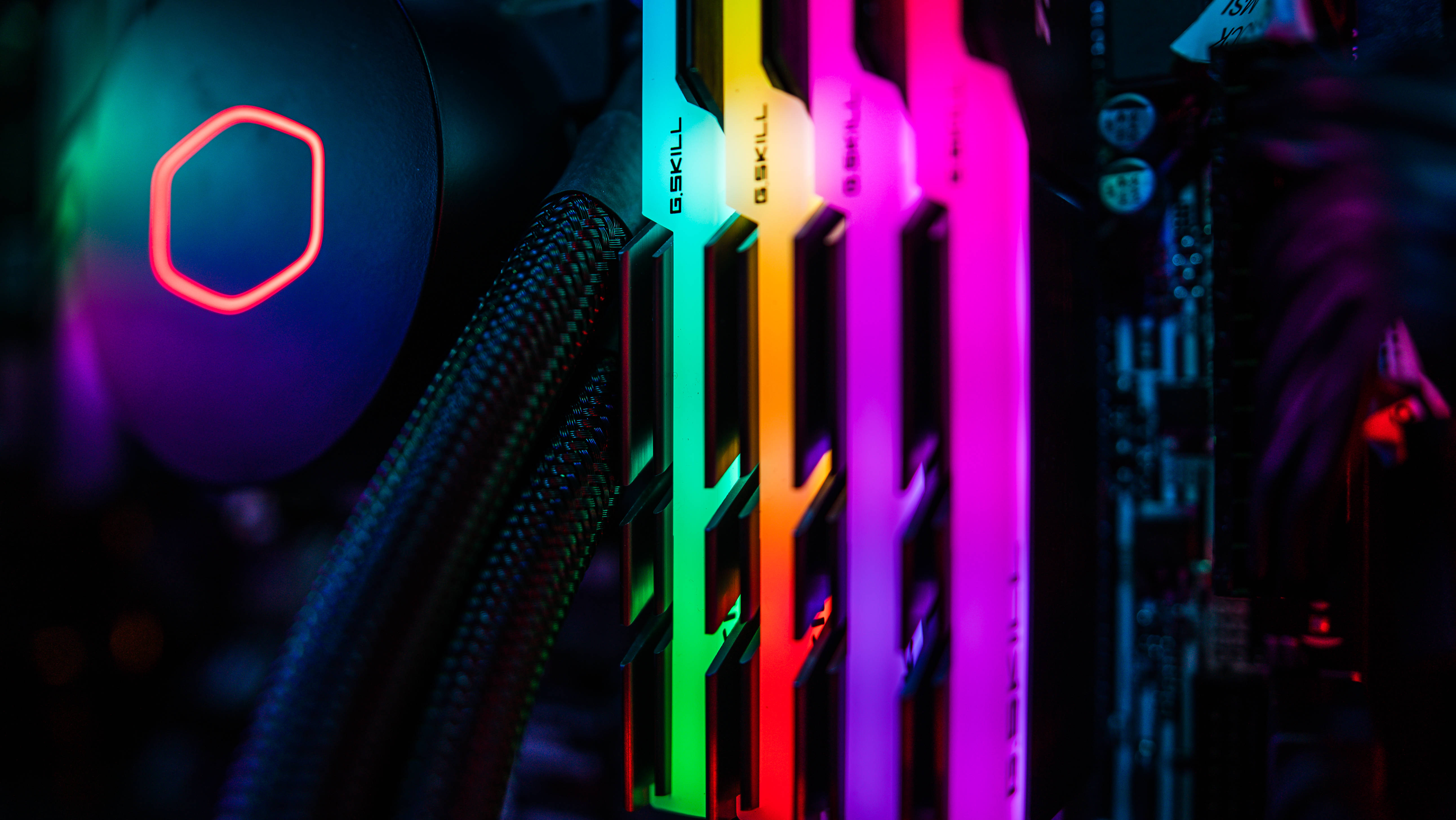 Motherboard 桌布 壁紙 — 色彩繽紛的彩虹LED G.SKILL RAM模組在黑色電腦機箱中發光，背景有一個紅色六角形風扇。