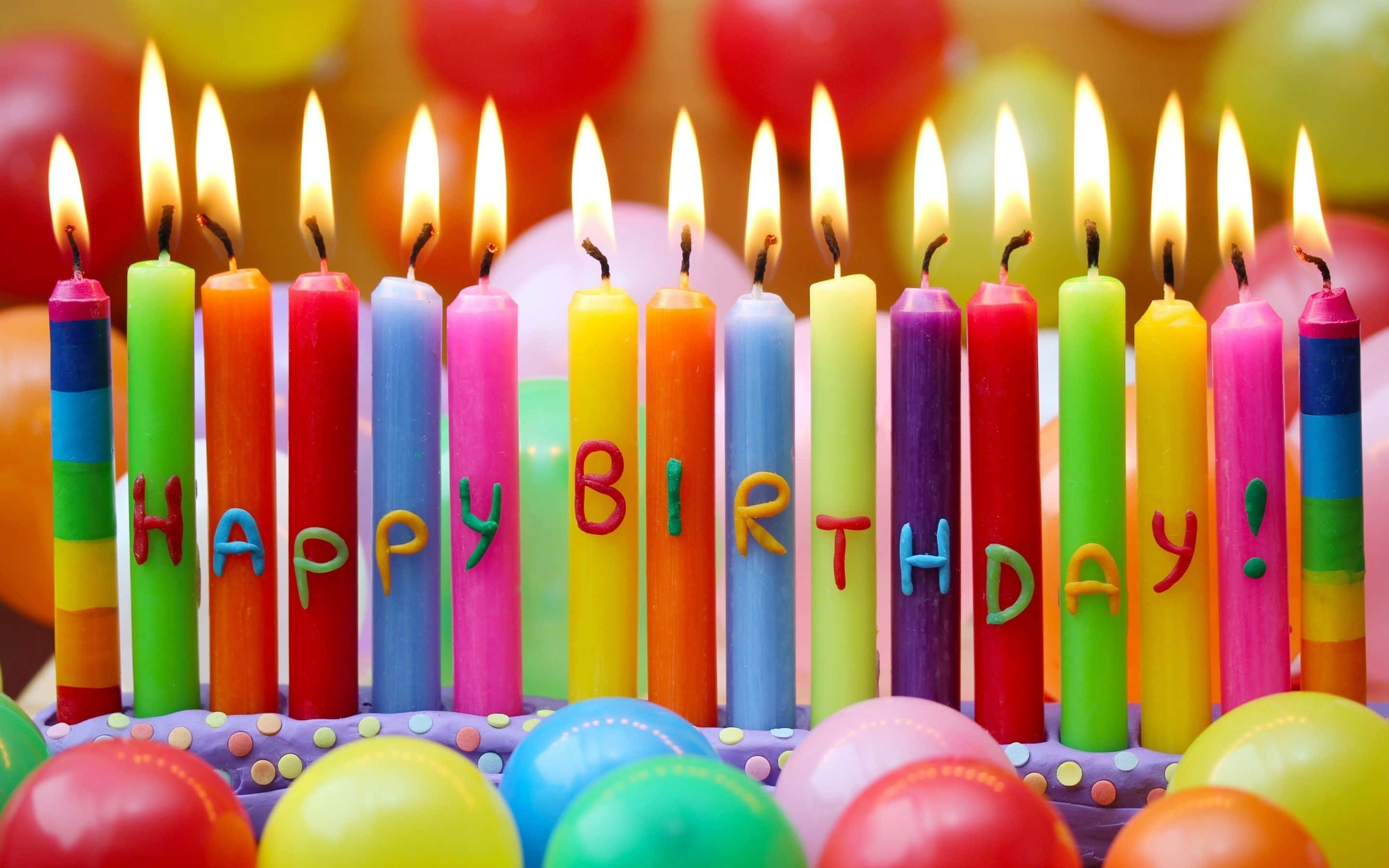 生日快樂 桌布 壁紙 — 色彩繽紛的彩虹生日蠟燭拼出「生日快樂」，燭光在色彩繽紛的蛋糕上搖曳，周圍環繞著氣球。