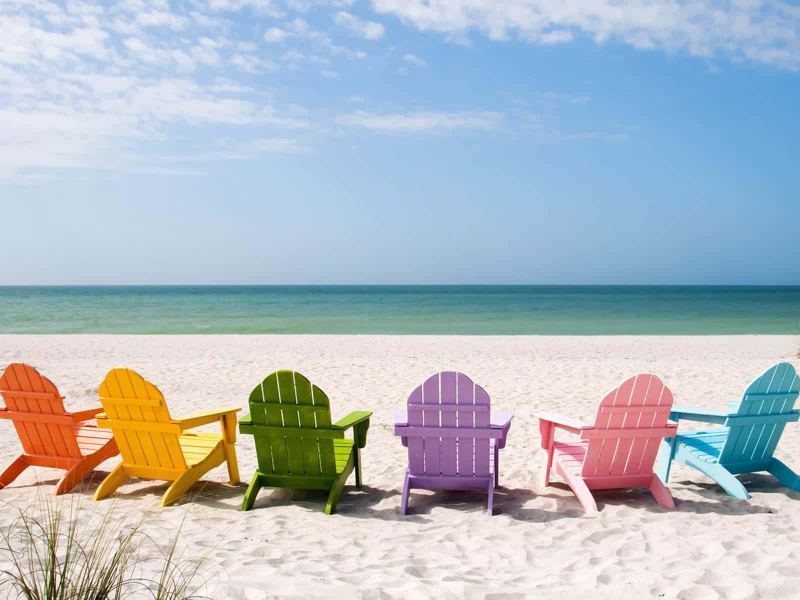 Beach Scene 桌布 壁紙 — 色彩繽紛的彩虹阿迪朗達克椅面向碧綠色的海洋，在晴朗的藍天下，陽光燦爛的海灘上。