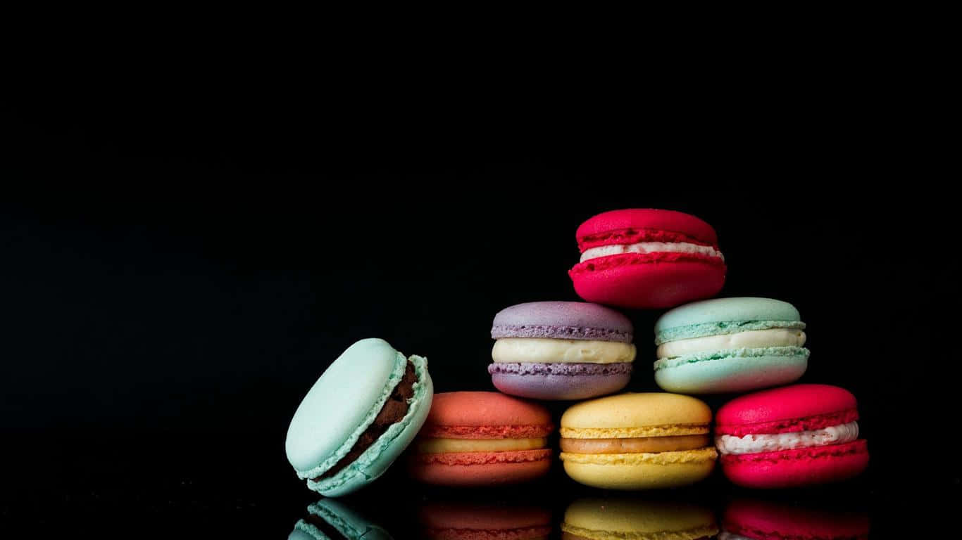 1366x768 Desserts 桌布 壁紙 — 色彩繽紛的彩虹馬卡龍堆疊成金字塔，置於純黑背景上，帶有光澤反射。