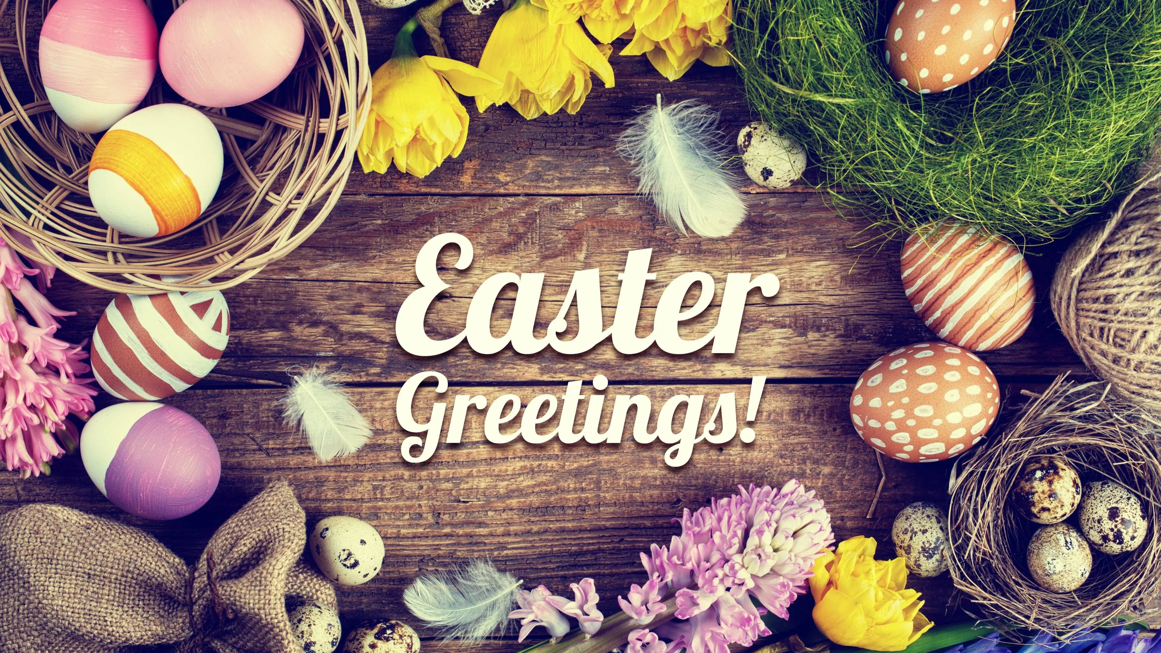 Easter 桌布 壁紙 — 色彩繽紛的復活節蛋和花朵擺放在質樸的木桌上，帶有「Easter Greetings!」文字。