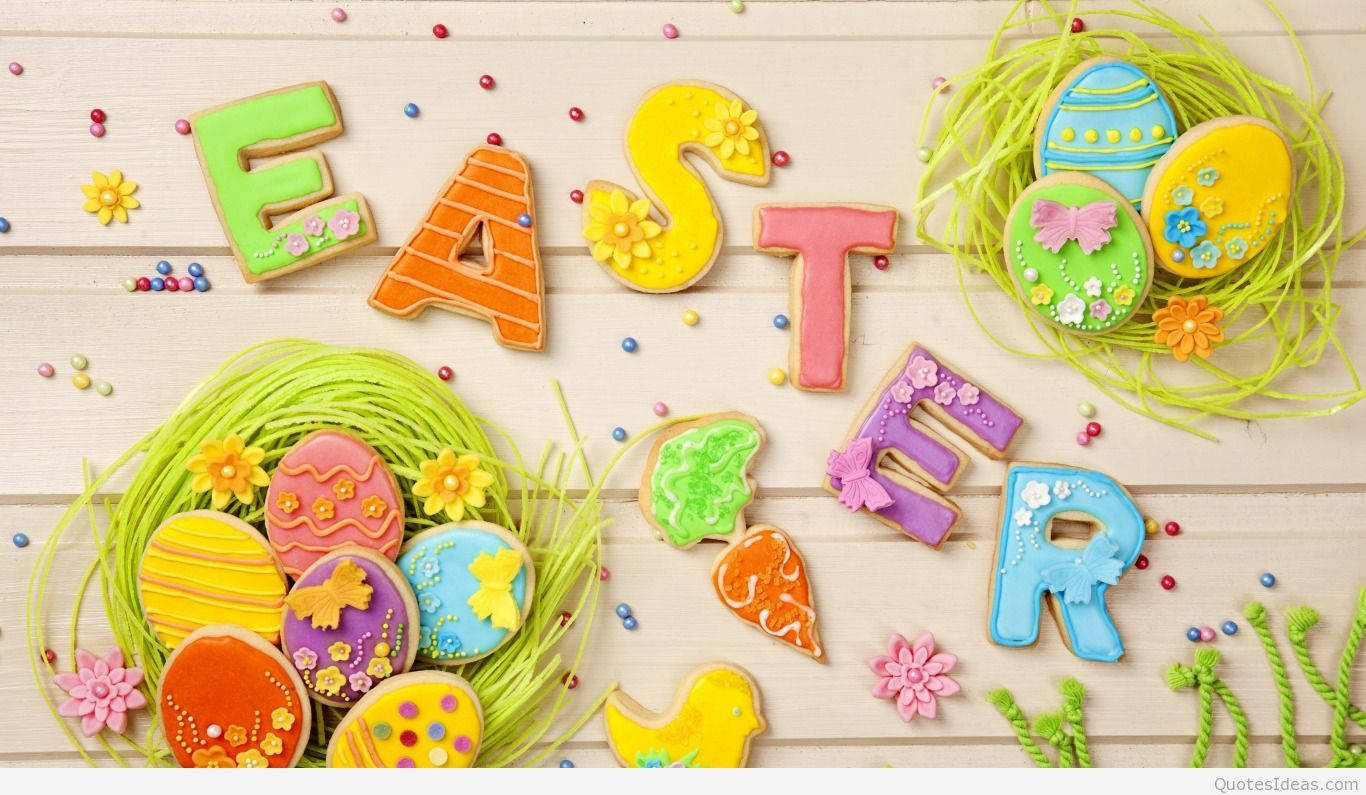 Happy Easter 桌布 壁紙 — 色彩繽紛的復活節餅乾，形狀像字母和雞蛋，藏在木質表面上的綠色草叢中。