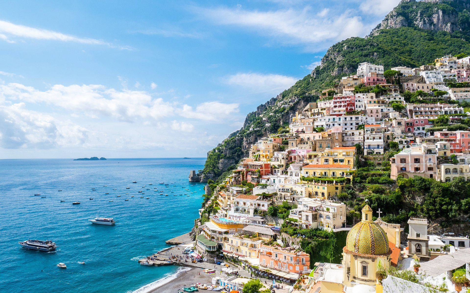 Capri 桌布 壁紙 — 色彩繽紛的懸崖小鎮波西塔諾沿著翠綠的山坡傾瀉而下，匯入湛藍的地中海，上方是明亮的藍天。