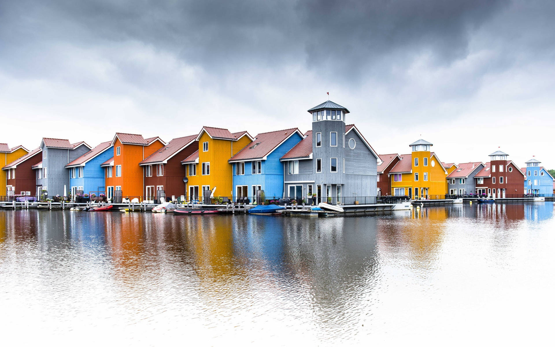 Netherlands 桌布 壁紙 — 色彩繽紛的房屋排列在平靜的海濱，天空戲劇性地多雲，水面上閃爍著倒影。