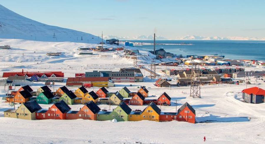 Svalbard 桌布 壁紙 — 色彩繽紛的房屋點綴著冰雪覆蓋的北極小鎮，旁邊是冰封的海洋，天空湛藍清澈。