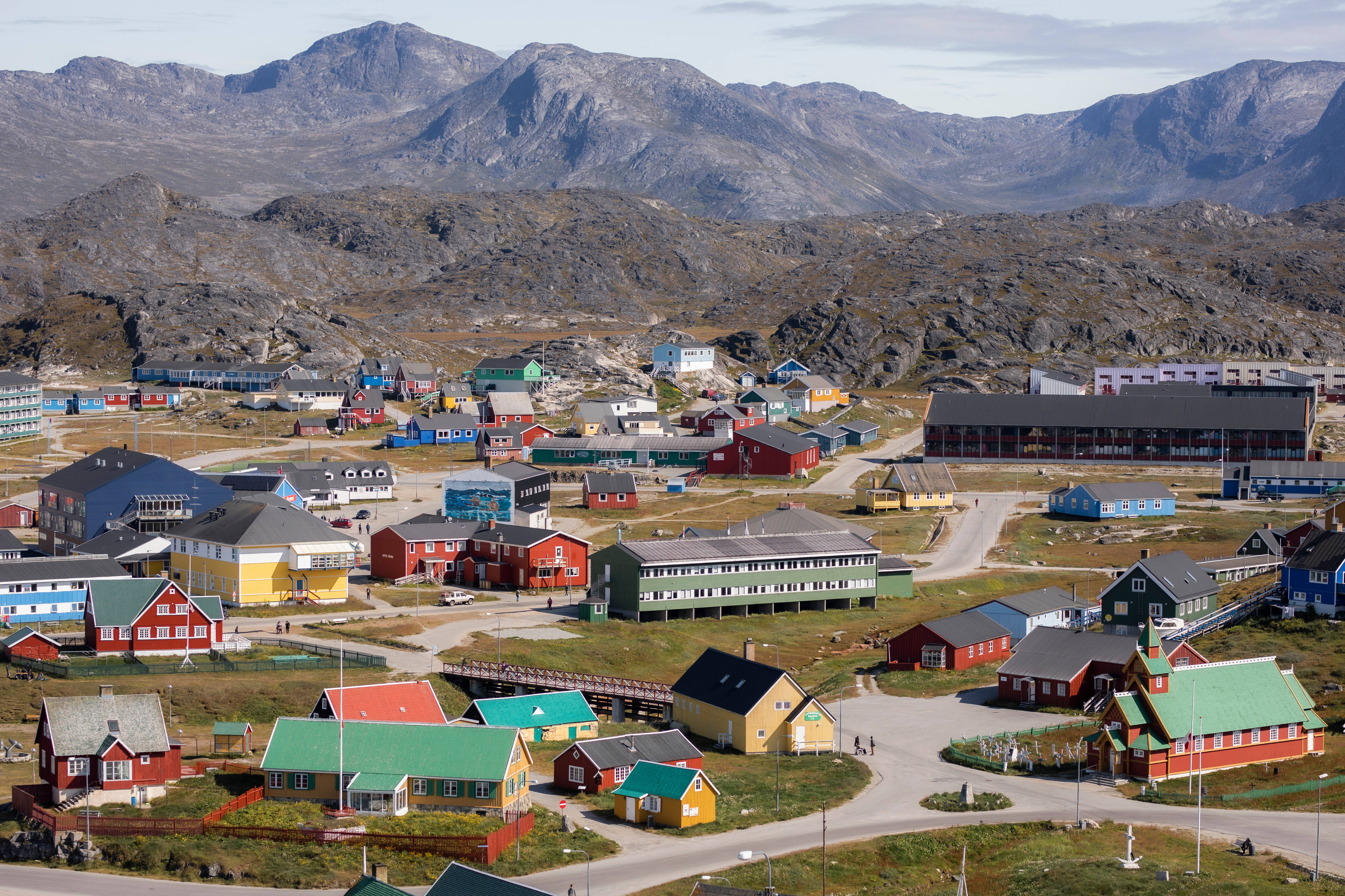 Greenland 桌布 壁紙 — 色彩繽紛的房屋點綴著崎嶇的北極小鎮，坐落在灰濛濛的山腳下，天空明亮。