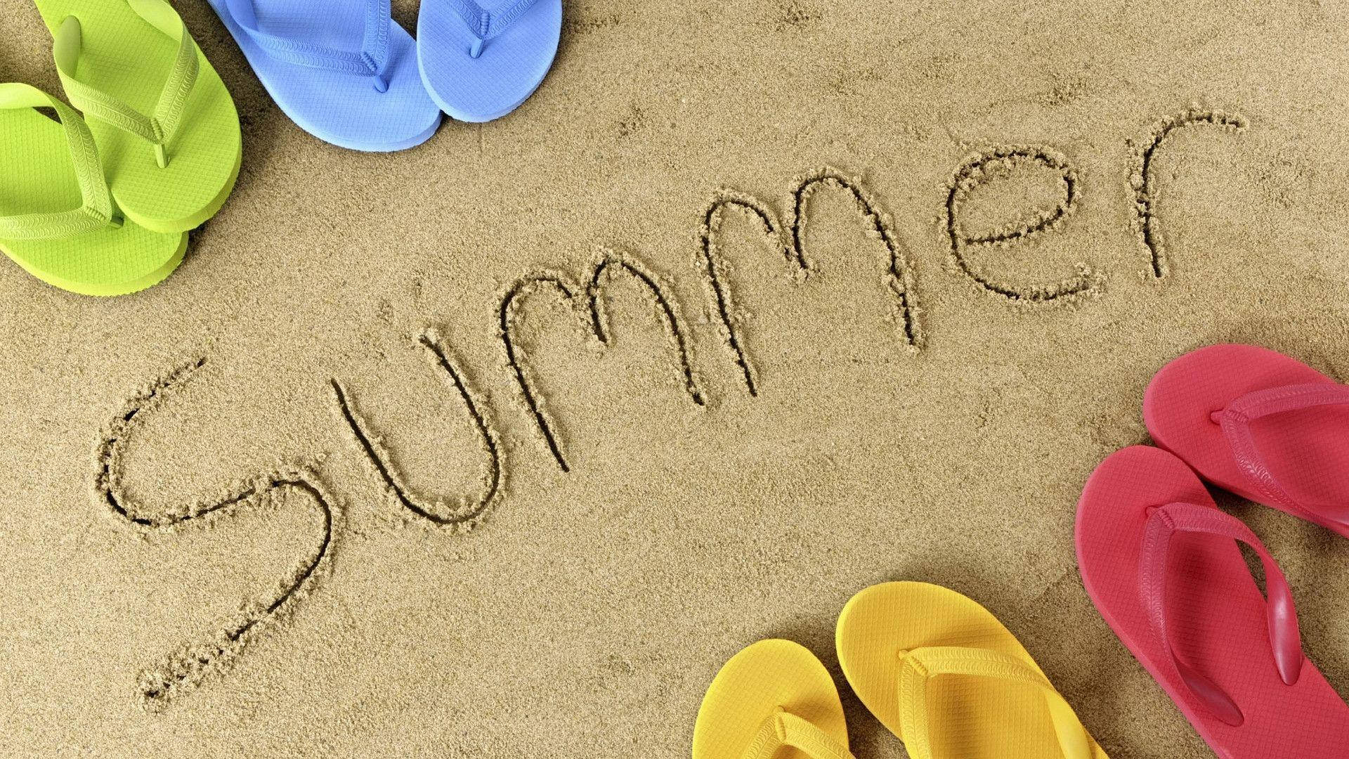 夏季 桌布 壁紙 — 色彩繽紛的拖鞋圍繞著沙灘上寫的「Summer」一詞，營造出明亮的沙灘度假氛圍。