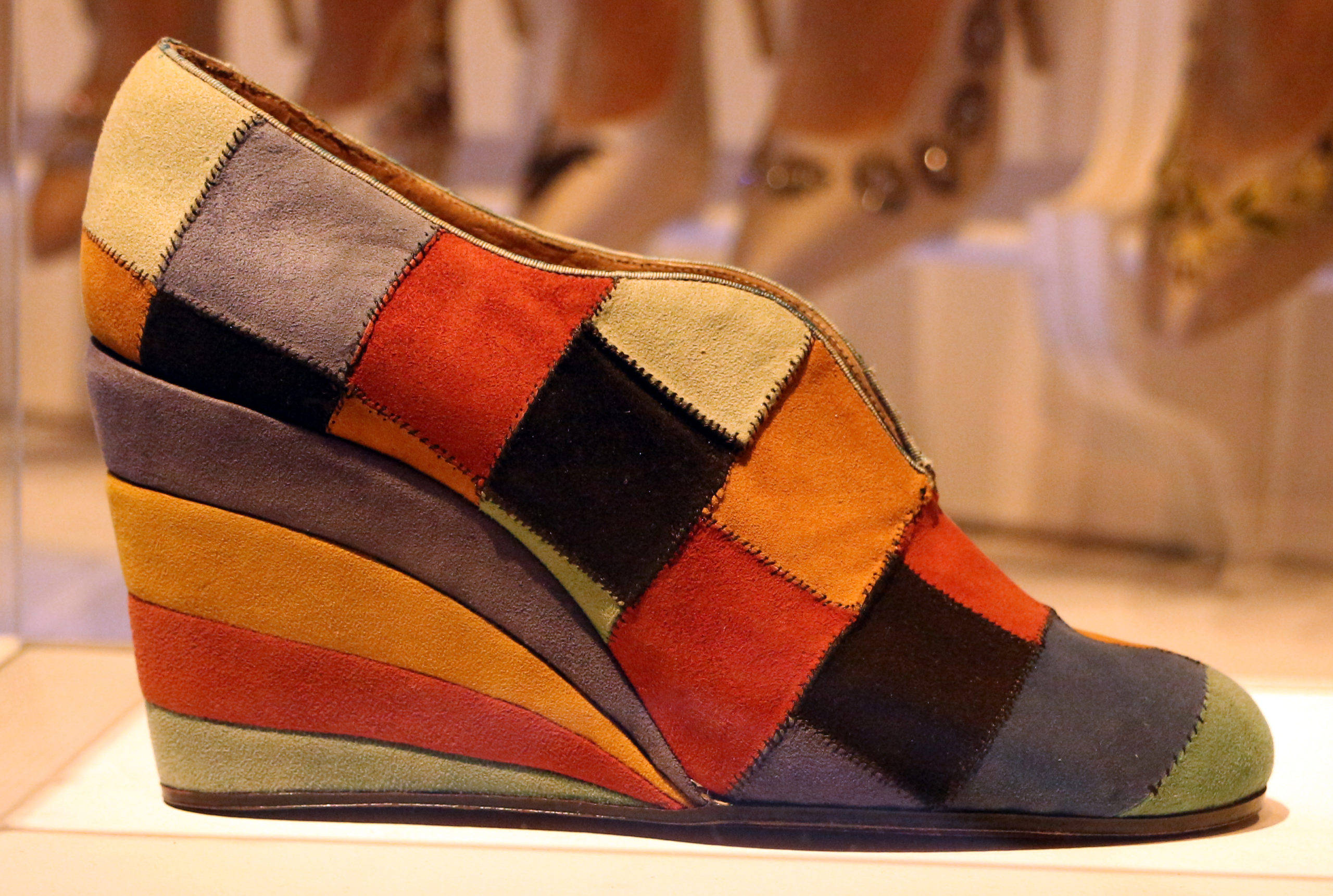 Ferragamo 桌布 壁紙 — 色彩繽紛的拼布坡跟鞋，採用紅色、橙色、黑色和米色麂皮面板，展示在白色底座上。