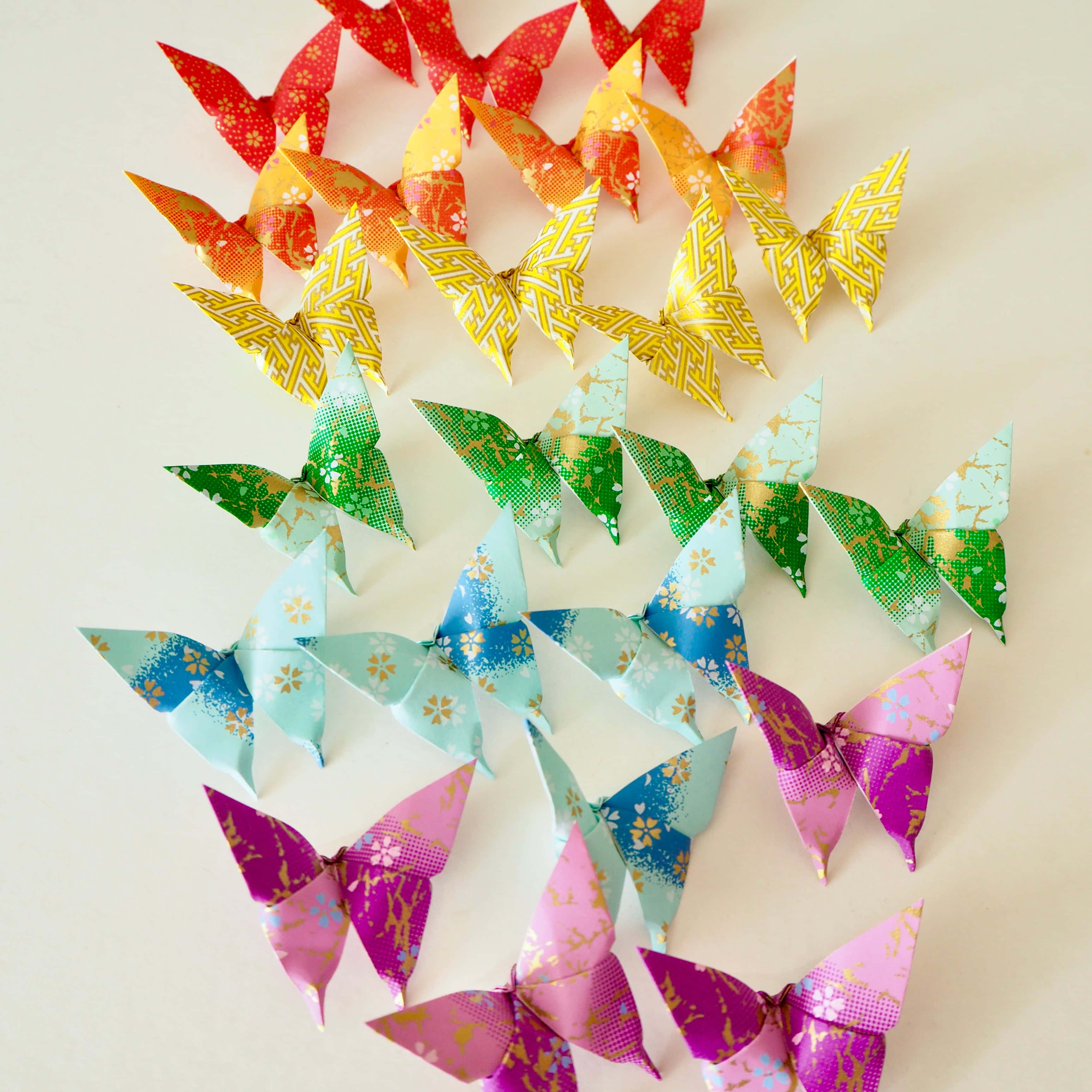 Butterfly Origami 桌布 壁紙 — 色彩繽紛的摺紙蝴蝶在柔和米色背景上排列成彩虹行。