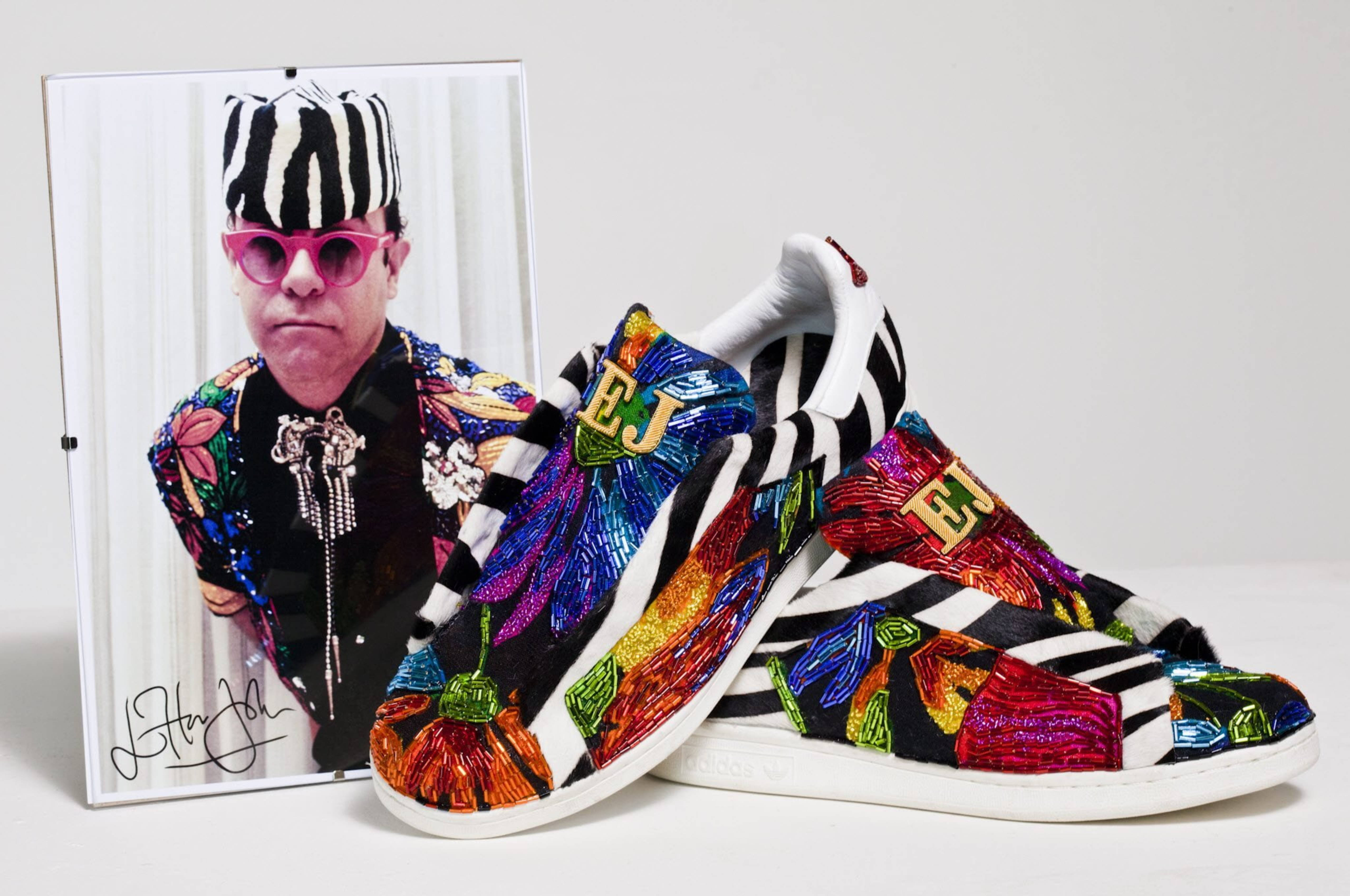 Elton John 桌布 壁紙 — 色彩繽紛的斑馬紋和花卉刺繡運動鞋，旁邊放著一張艾爾頓·約翰穿著相配服裝的裱框照片。