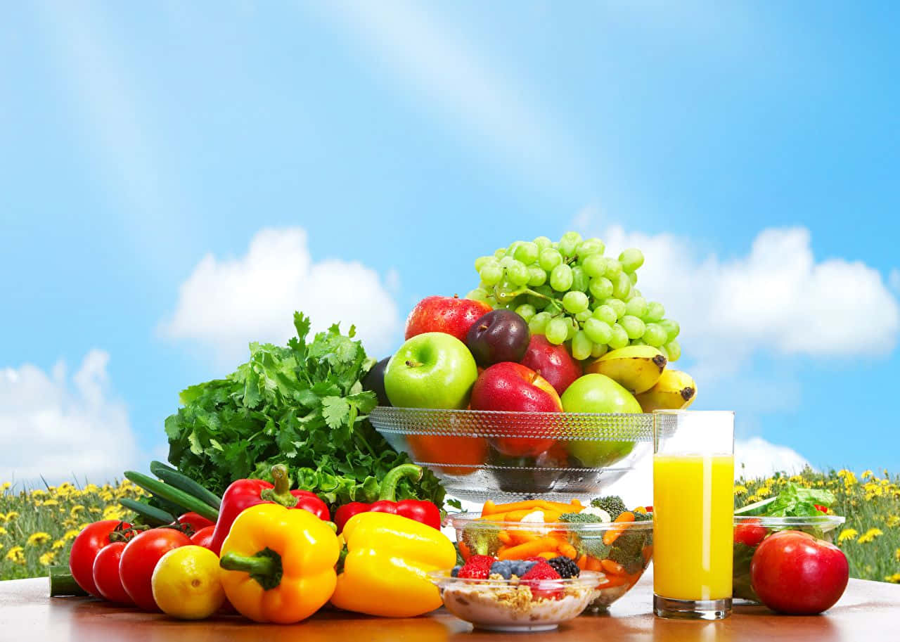 pepper 桌布 壁紙 — 色彩繽紛的新鮮水果、蔬菜和果汁擺放在木桌上，背景是明亮的藍天和蓬鬆的白雲。