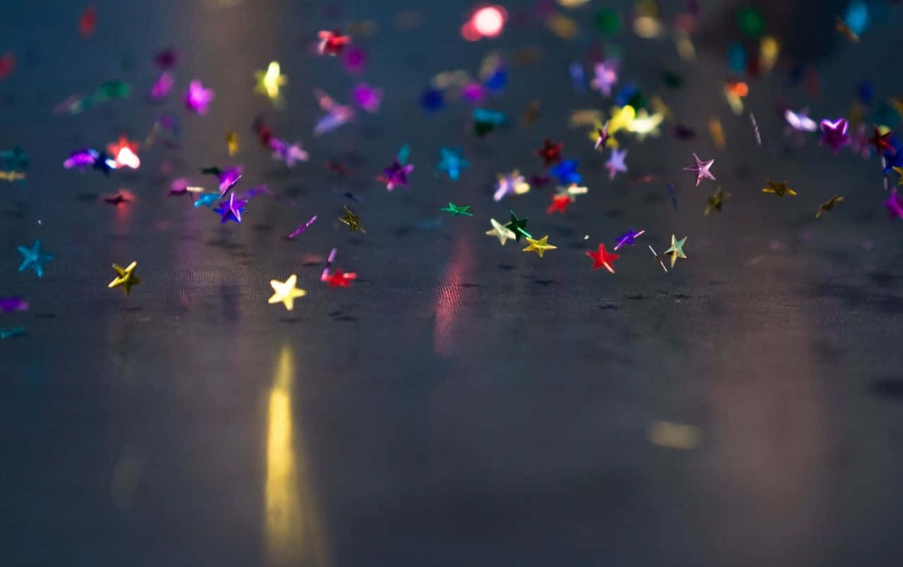 Cheerful 桌布 壁紙 — 色彩繽紛的星形紙屑在溫暖燈光下漂浮並閃爍在深色反光表面上。
