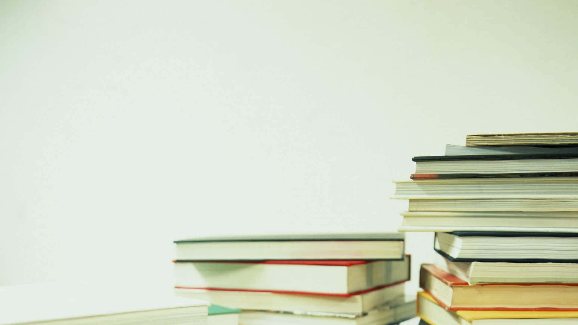 Educated 桌布 壁紙 — 色彩繽紛的書脊書堆放在柔和的白色背景下的平坦表面上。