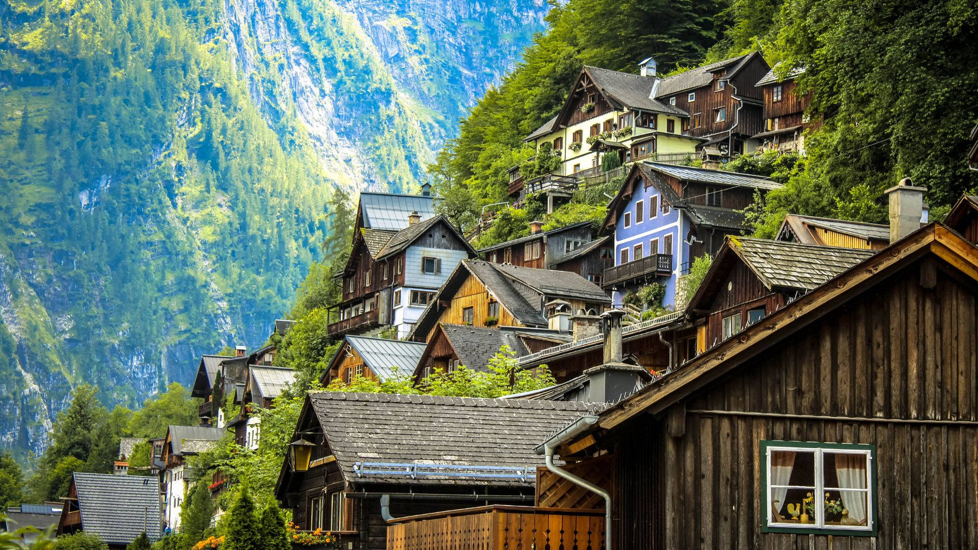 高清 桌布 壁紙 — 色彩繽紛的木屋在明亮的日光下依附在陡峭的森林山坡上。