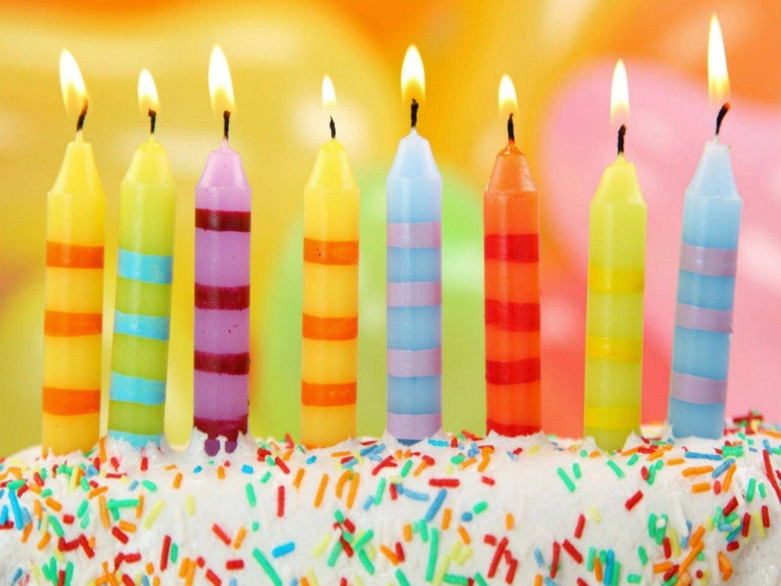 蛋糕 桌布 壁紙 — 色彩繽紛的條紋生日蠟燭在鋪滿彩色糖粒的白色糖霜蛋糕上閃爍。