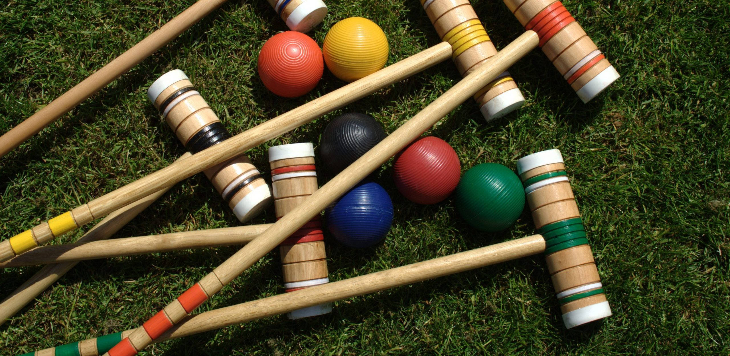 ball 桌布 壁紙 — 色彩繽紛的槌球槌和球散落在充滿活力的綠色草地上，陽光明媚。
