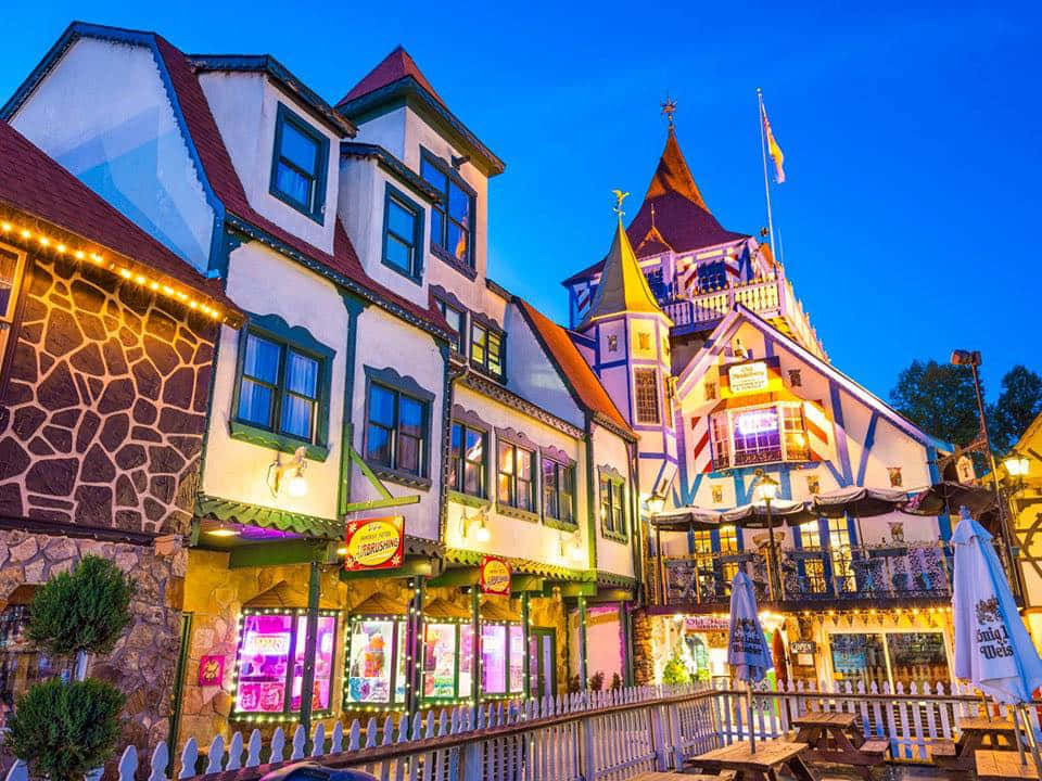 Village 桌布 壁紙 — 色彩繽紛的歐式建築在迷人的小鎮廣場上，溫暖的燈光在深藍色的暮色天空中閃耀。