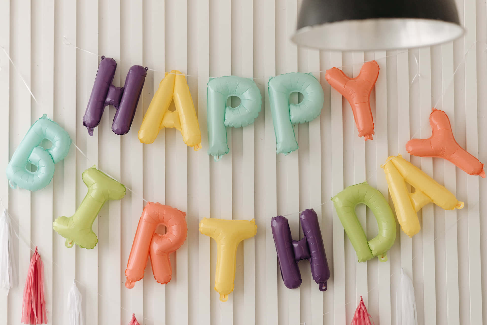 生日快樂 桌布 壁紙 — 色彩繽紛的氣球字母在白色板條牆上拼出「HAPPY BIRTHDAY」，下方有一盞吊燈。