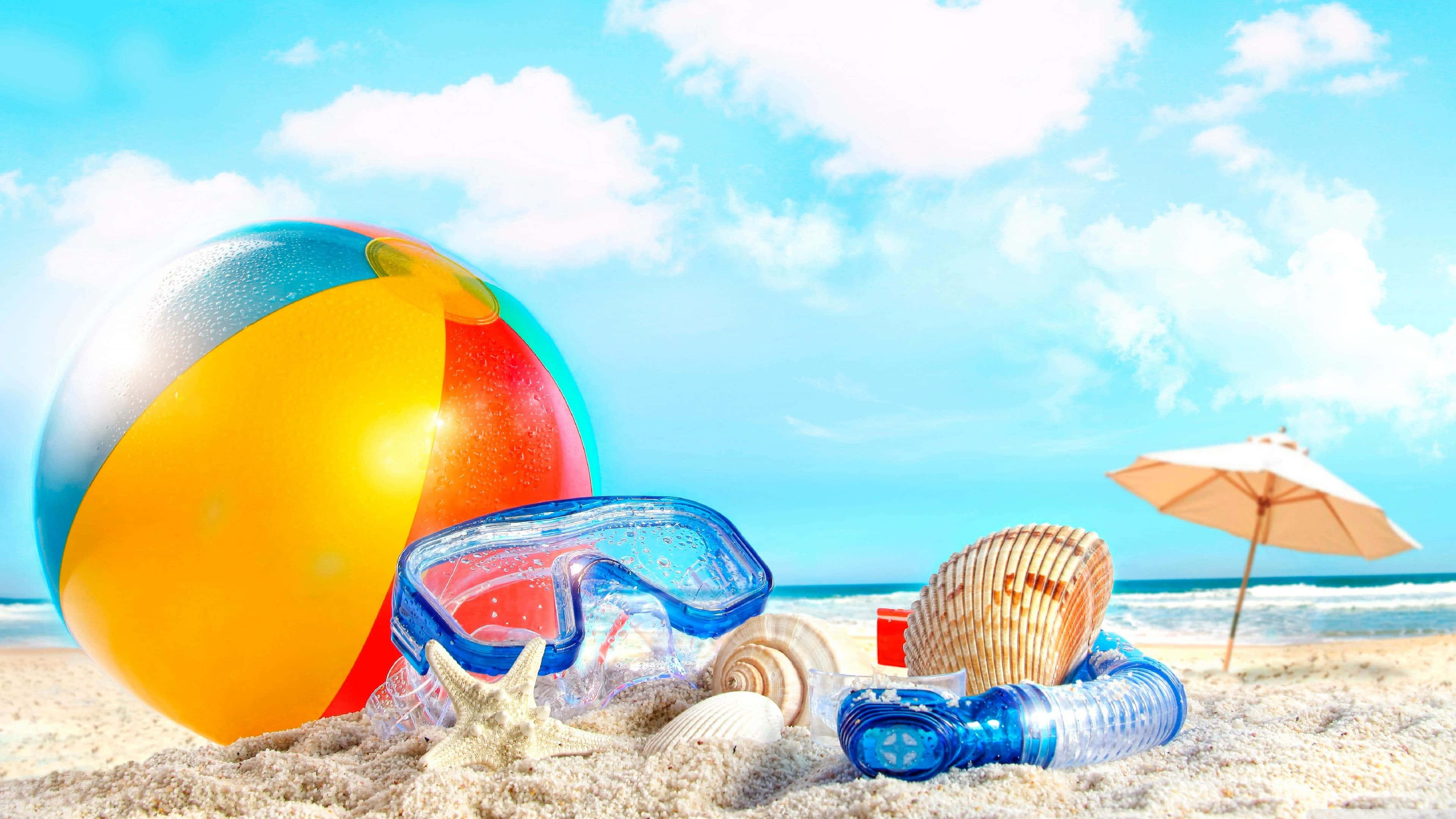 夏天 桌布 壁紙 — 色彩繽紛的沙灘球、浮潛面罩和貝殼放在金色沙灘上，背景是晴朗藍天和 fluffy 白雲。