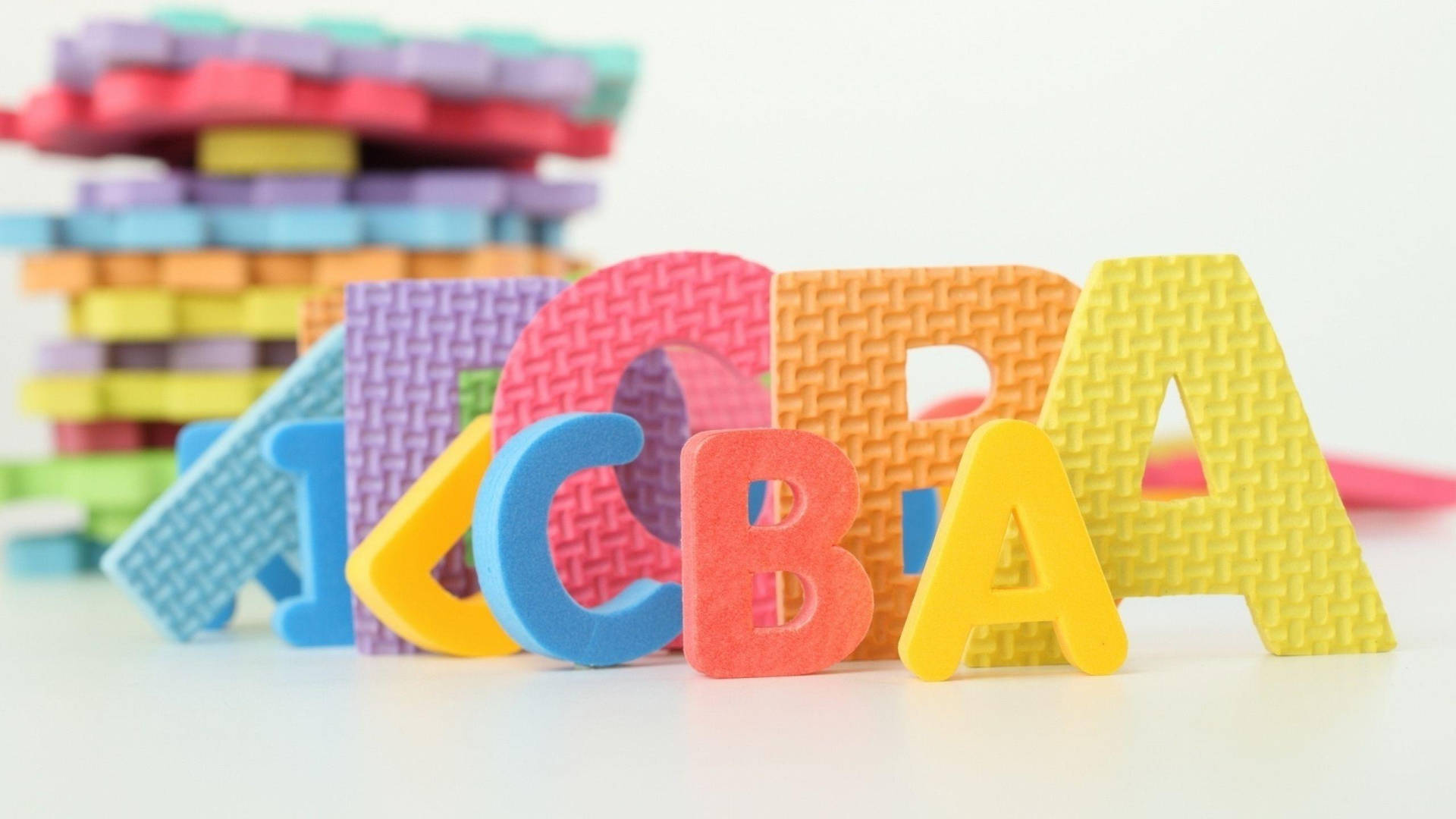 字母動畫 桌布 壁紙 — 色彩繽紛的泡沫字母拼出「CBA」，背景有堆疊的積木，置於白色表面上。