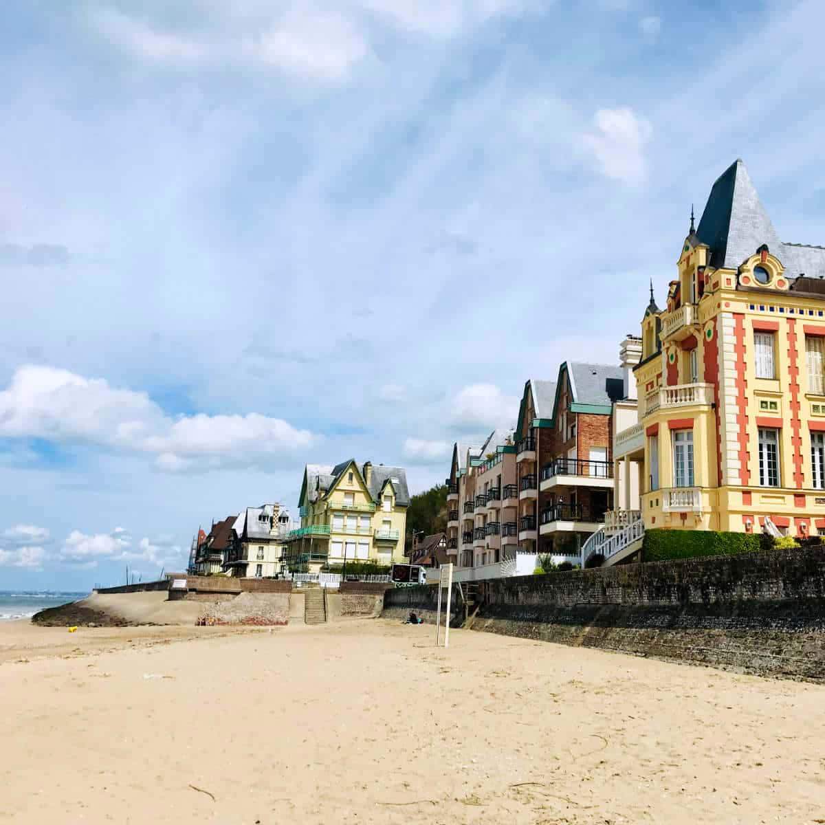 French Beach 桌布 壁紙 — 色彩繽紛的海邊建築物棲息在石牆上，下方是寬闊的沙灘，天空部分多雲。