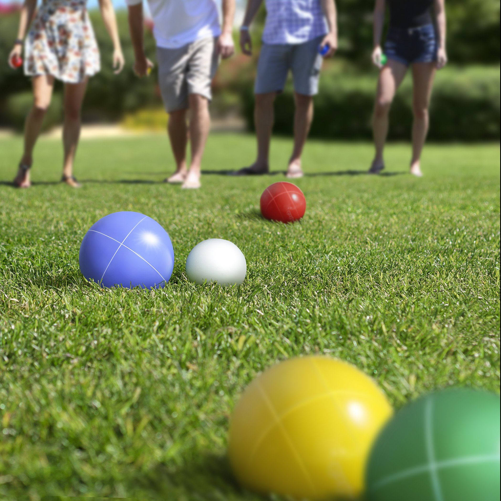 Grass 桌布 壁紙 — 色彩繽紛的滾球（Bocce）在茂盛綠草上靜置，模糊的玩家們正準備在陽光下進行戶外遊戲。