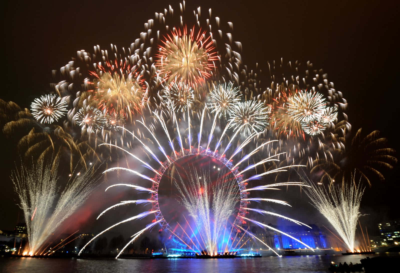New Years Eve 桌布 壁紙 — 色彩繽紛的煙火在倫敦眼上空於夜間綻放出耀眼圖案，倒映在下方水面上。