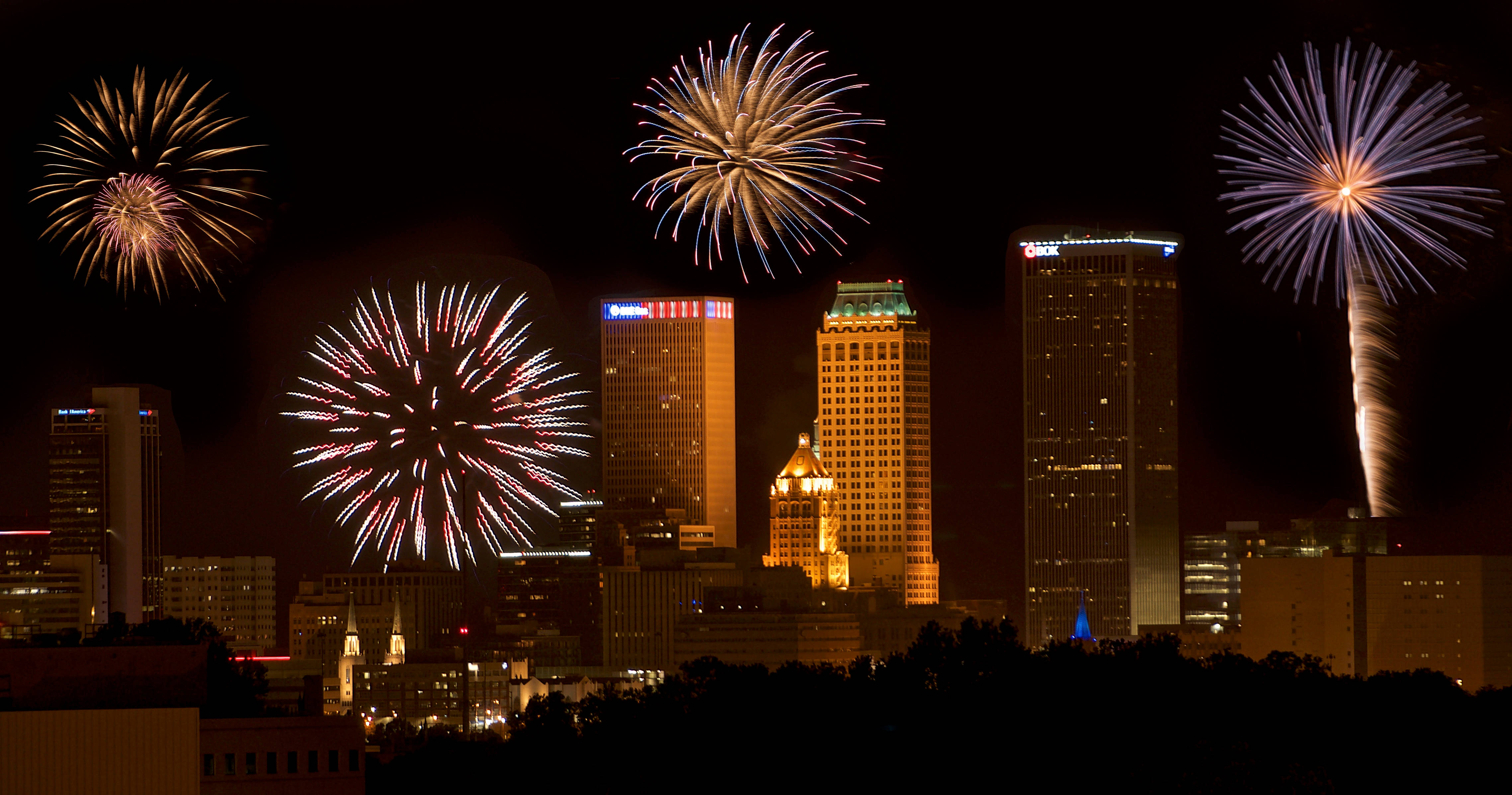 Fireworks 桌布 壁紙 — 色彩繽紛的煙火在夜間城市天際線上綻放出耀眼的光芒，用金色和多彩的光線照亮高聳的建築物。
