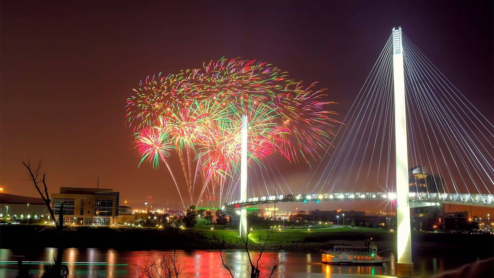 bridge 桌布 壁紙 — 色彩繽紛的煙火在夜間現代斜張橋上空綻放，下方城市燈光倒映在水面上。