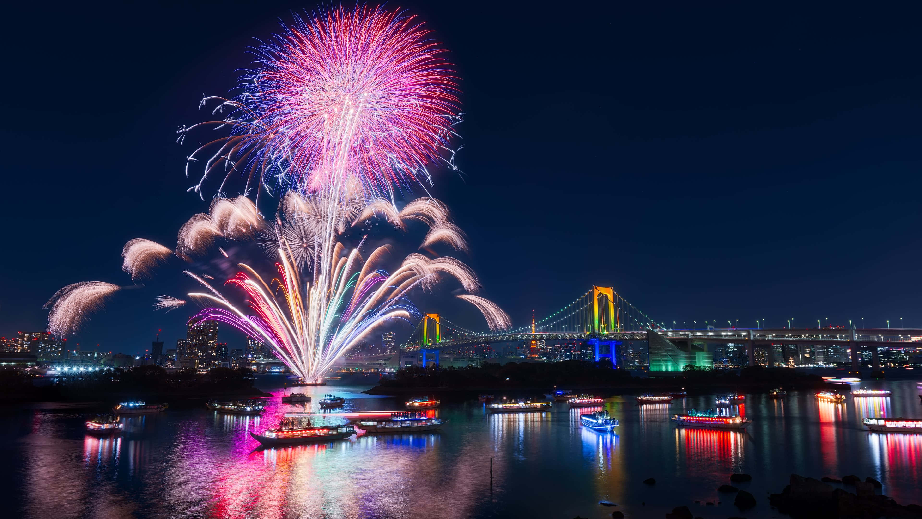 Fireworks 桌布 壁紙 — 色彩繽紛的煙火在東京灣上空綻放，照亮了彩虹橋和發光船隻上方的夜空。