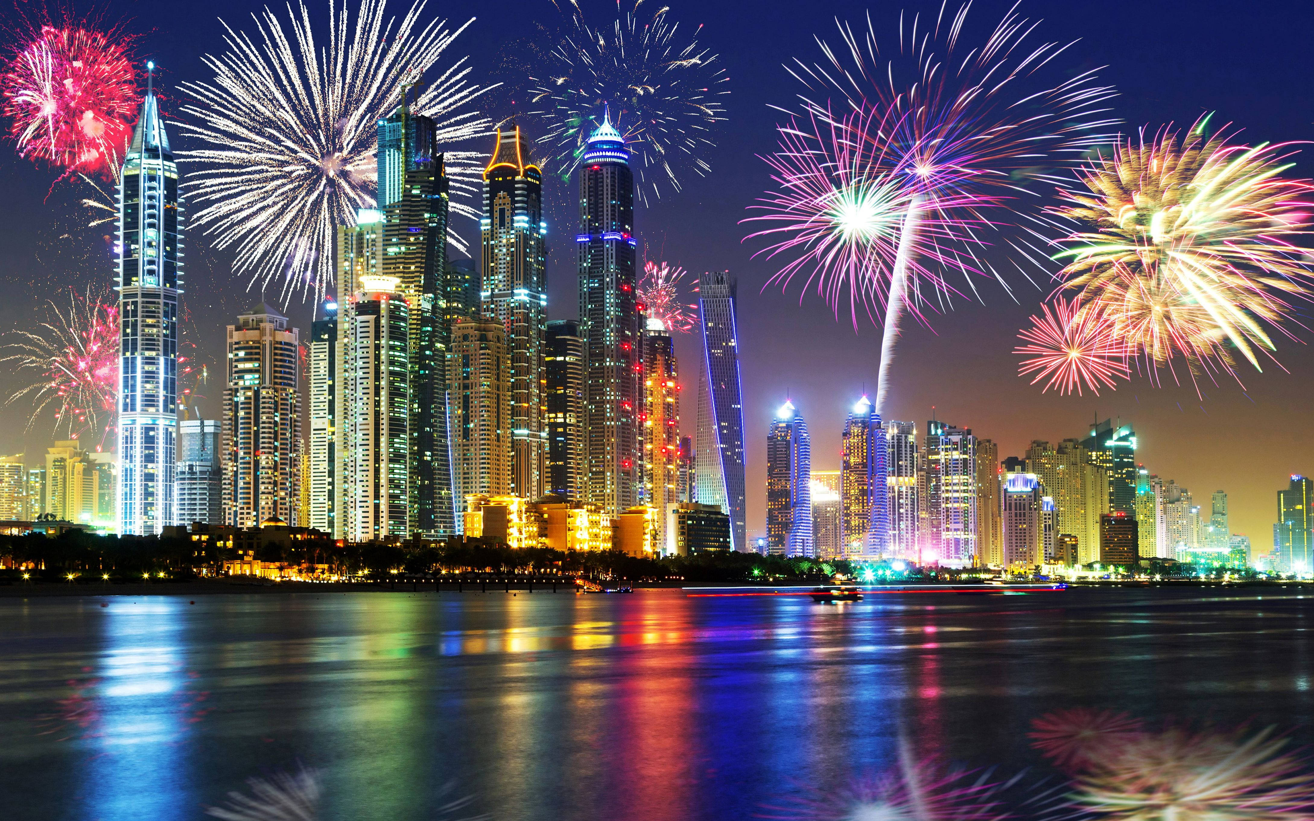 Arab 桌布 壁紙 — 色彩繽紛的煙火在閃爍的未來城市天際線上空綻放，倒映在夜晚平靜的水面上。