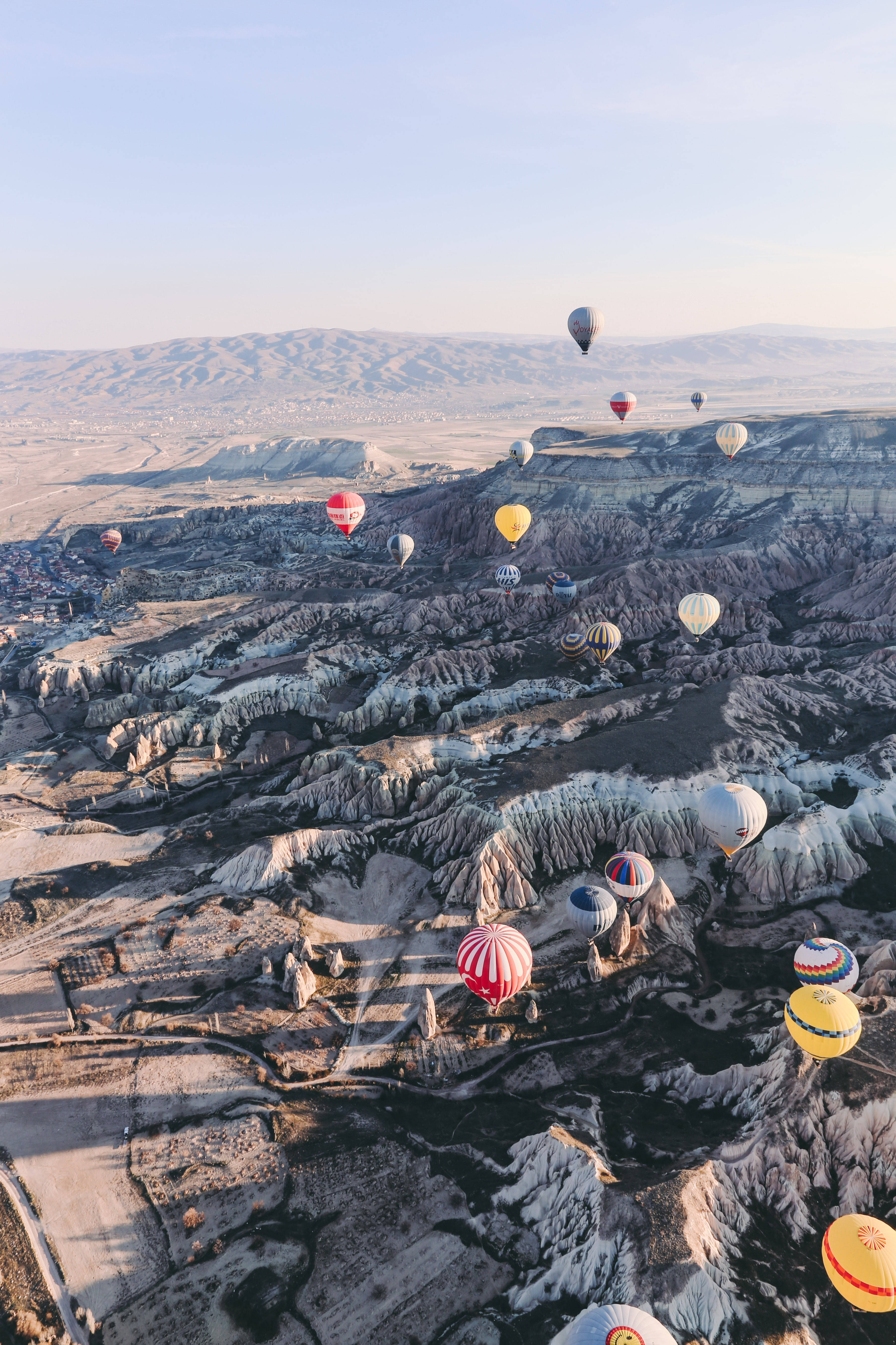 Cappadocia 桌布 壁紙 — 色彩繽紛的熱氣球在卡帕多奇亞崎嶇的岩石地貌上空飄浮，背景是清澈的藍天。