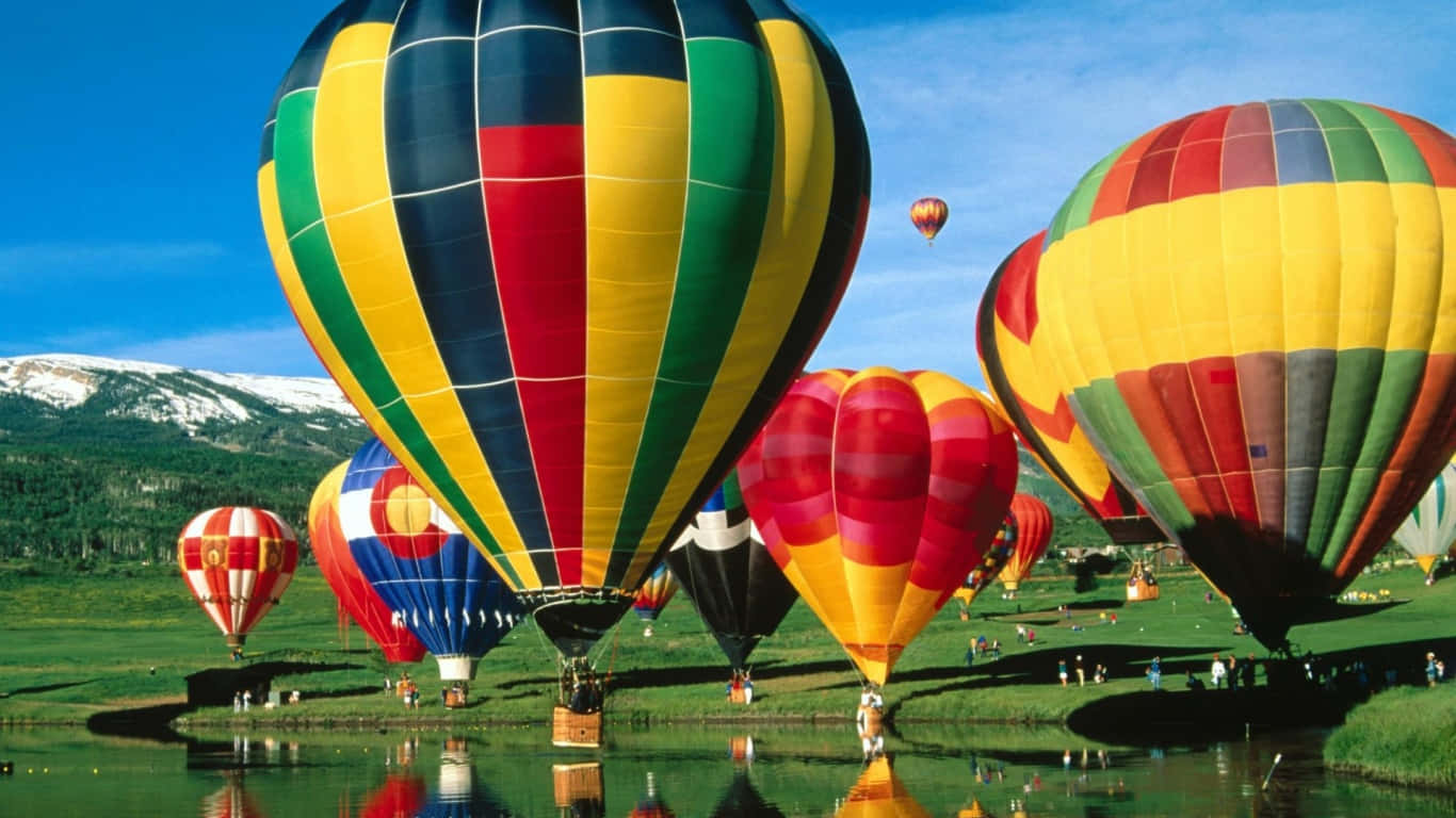 Hot Air Balloon 桌布 壁紙 — 色彩繽紛的熱氣球在彩虹色調中漂浮在寧靜的湖面上，背景是白雪覆蓋的山脈。