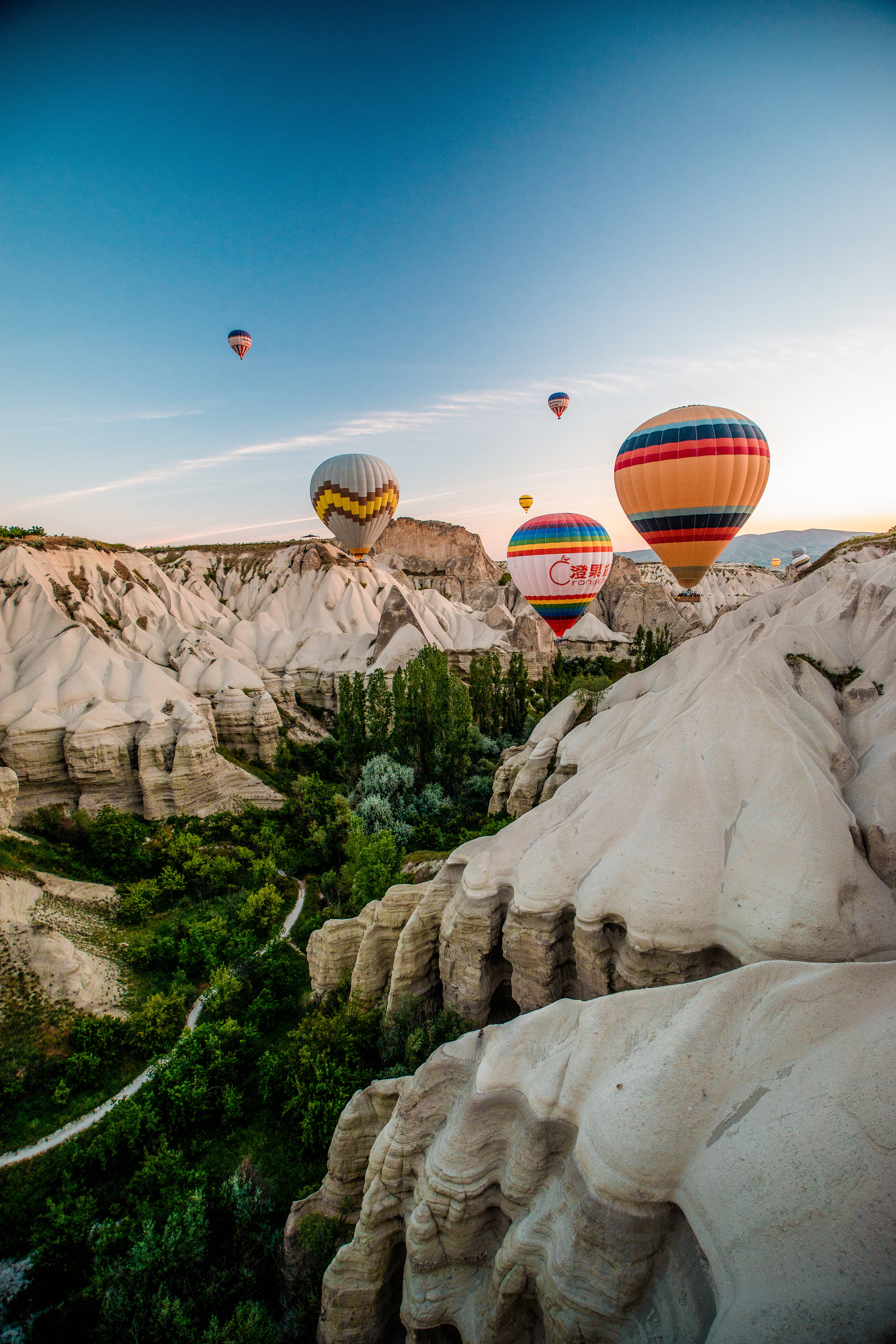Cappadocia 桌布 壁紙 — 色彩繽紛的熱氣球在日出時分，於晴朗藍天下飄過超現實的白色岩石地貌和綠色山谷。