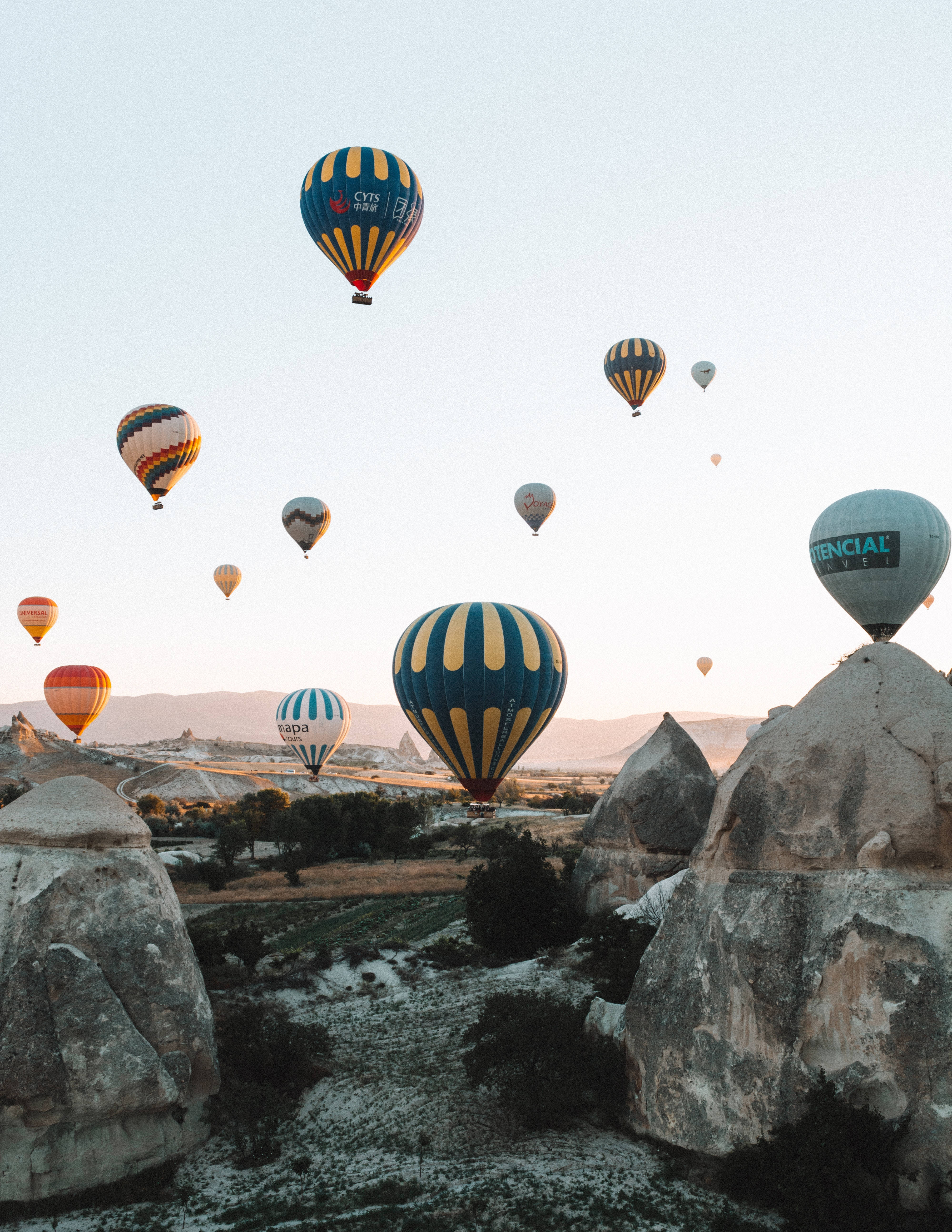 Cappadocia 桌布 壁紙 — 色彩繽紛的熱氣球在日出時柔和的金色天空下，飄浮在崎嶇的岩石地貌之上。