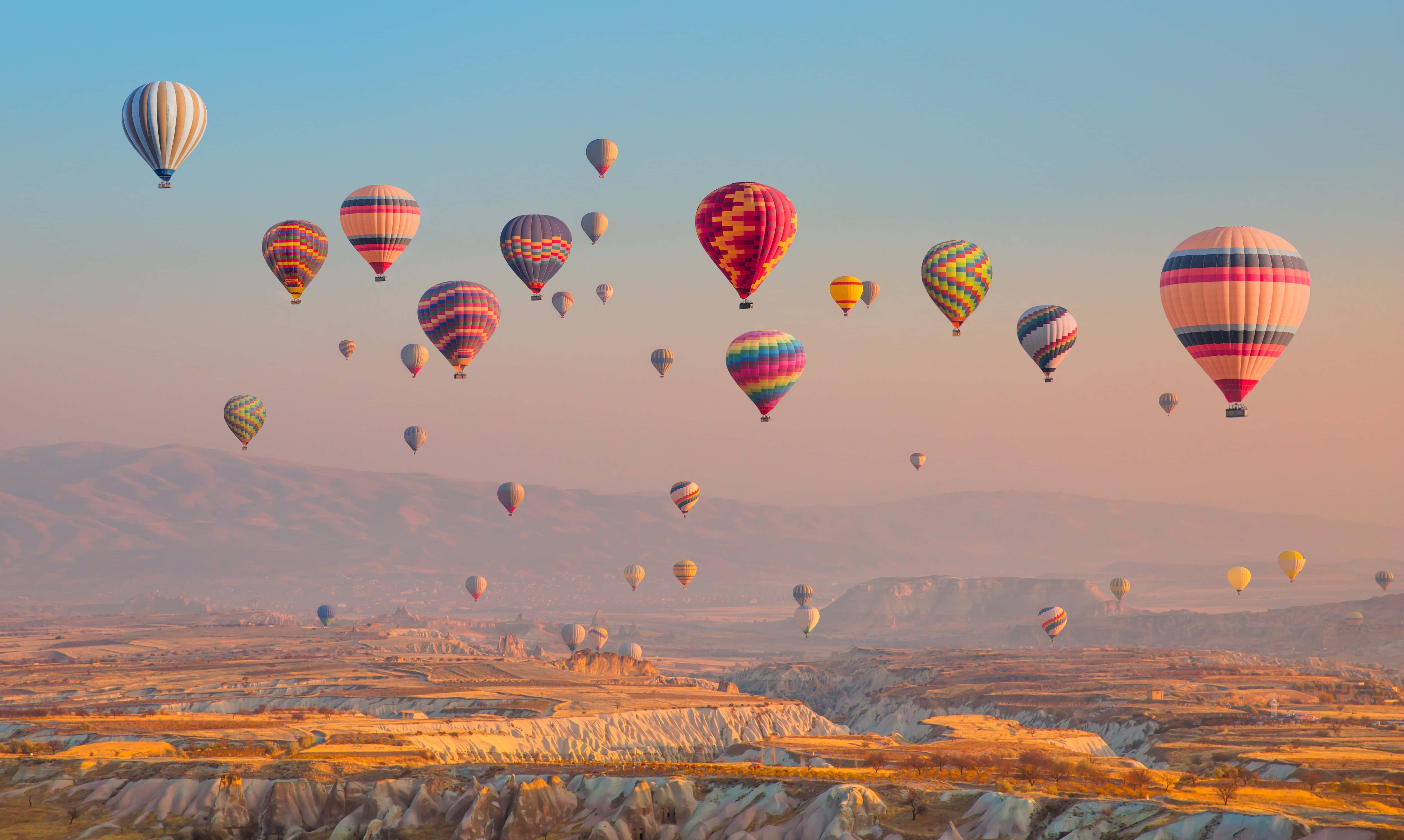Hot Air Balloon 桌布 壁紙 — 色彩繽紛的熱氣球在日出時飄過崎嶇的山谷，將溫暖的光線投射在岩石地形上。