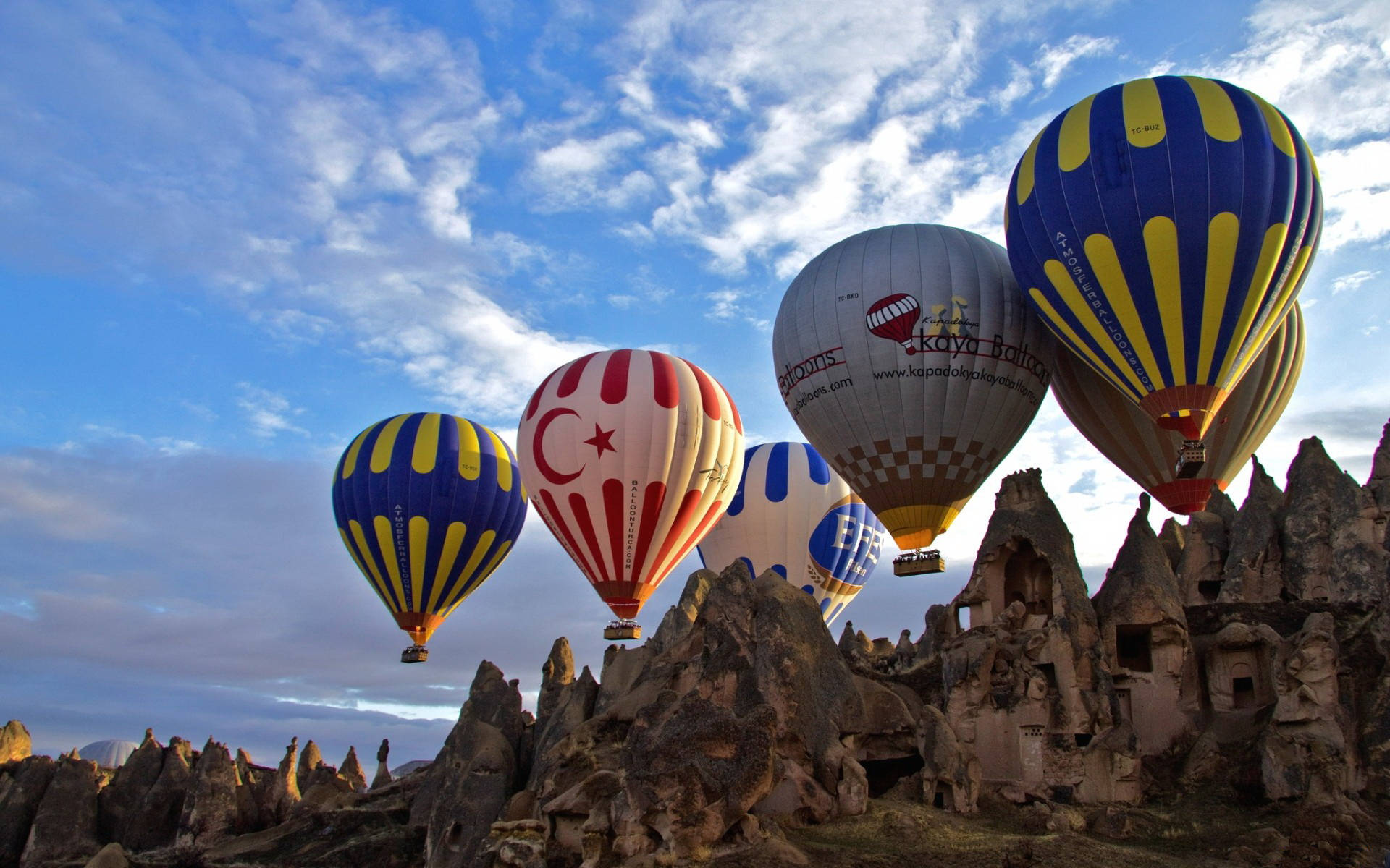 Hot Air Balloon 桌布 壁紙 — 色彩繽紛的熱氣球在明亮的藍天和散落的雲朵下，漂浮在崎嶇的仙女煙囪上方。