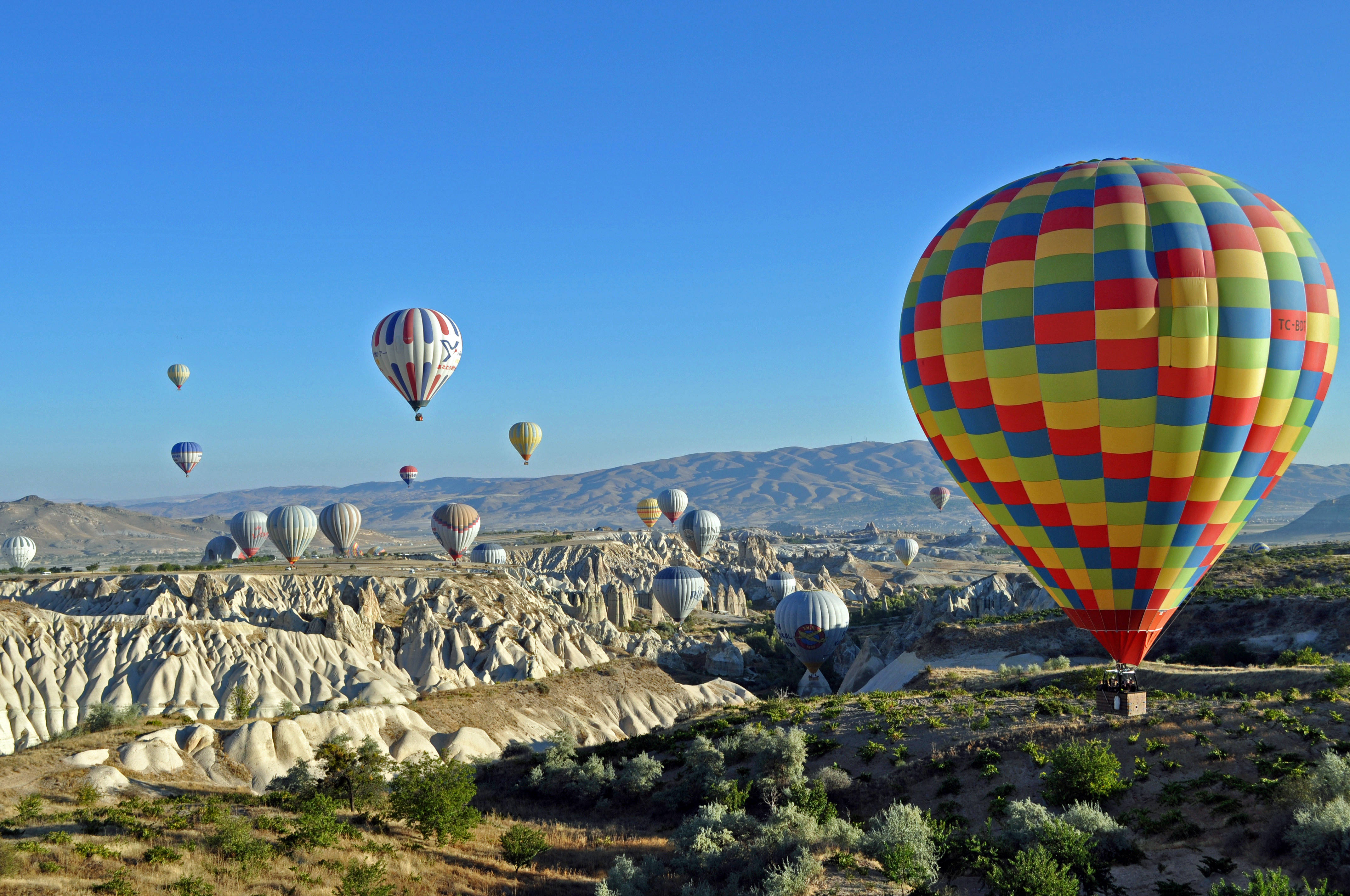 Cappadocia 桌布 壁紙 — 色彩繽紛的熱氣球在晴朗藍天下飄過超現實的岩石地貌。