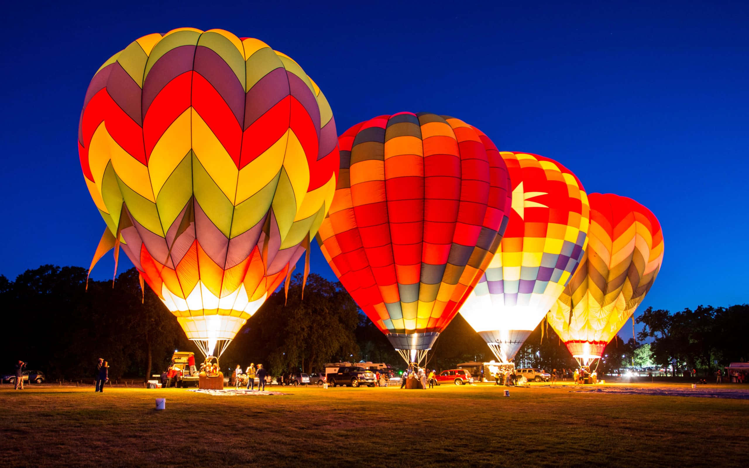 Hot Air Balloon 桌布 壁紙 — 色彩繽紛的熱氣球在深藍色暮色天空下，於草地上散發溫暖的光芒。