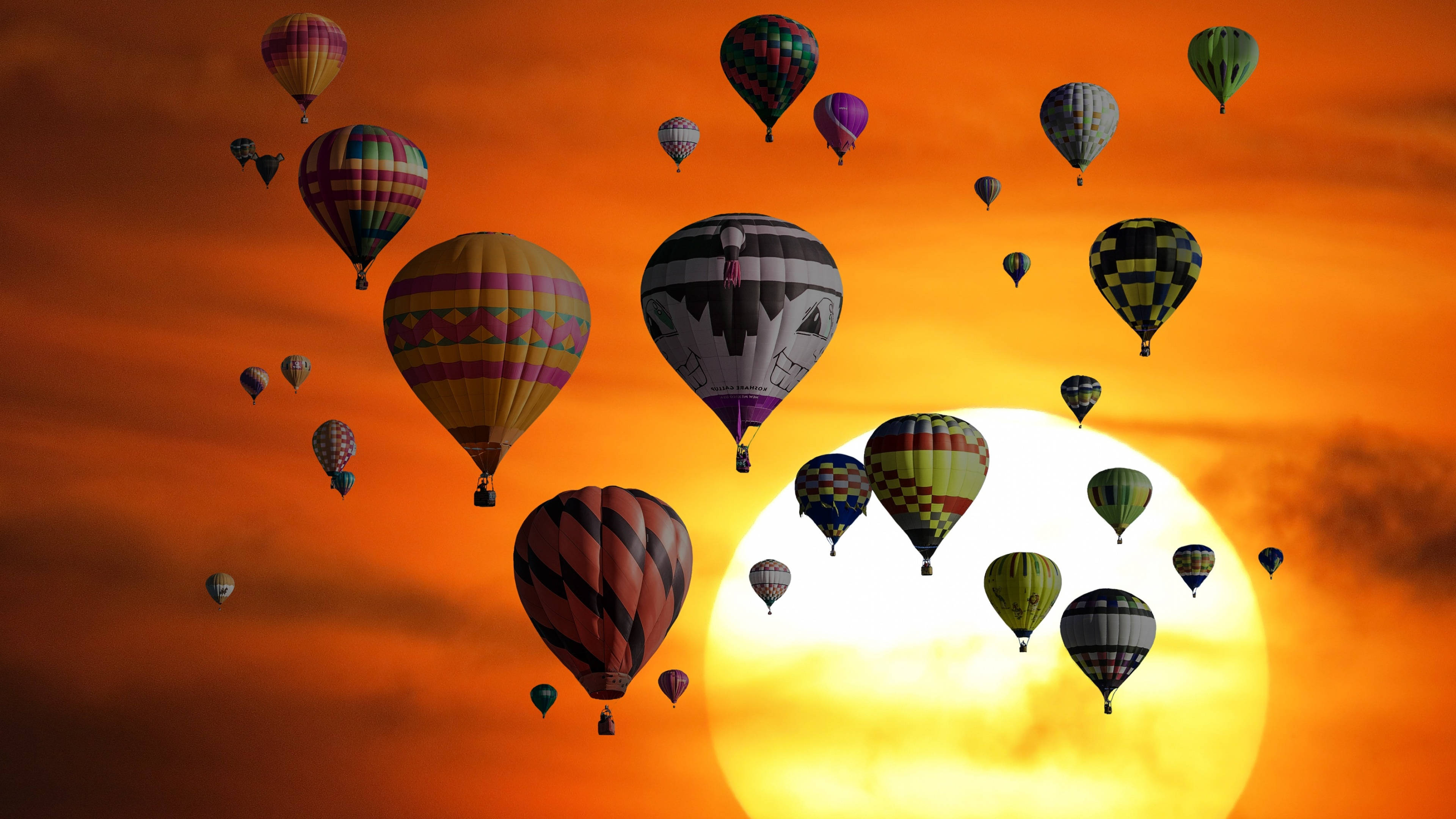 Hot Air Balloon 桌布 壁紙 — 色彩繽紛的熱氣球在火紅橙色的日落天空中飄移，中央有一顆發光的太陽。