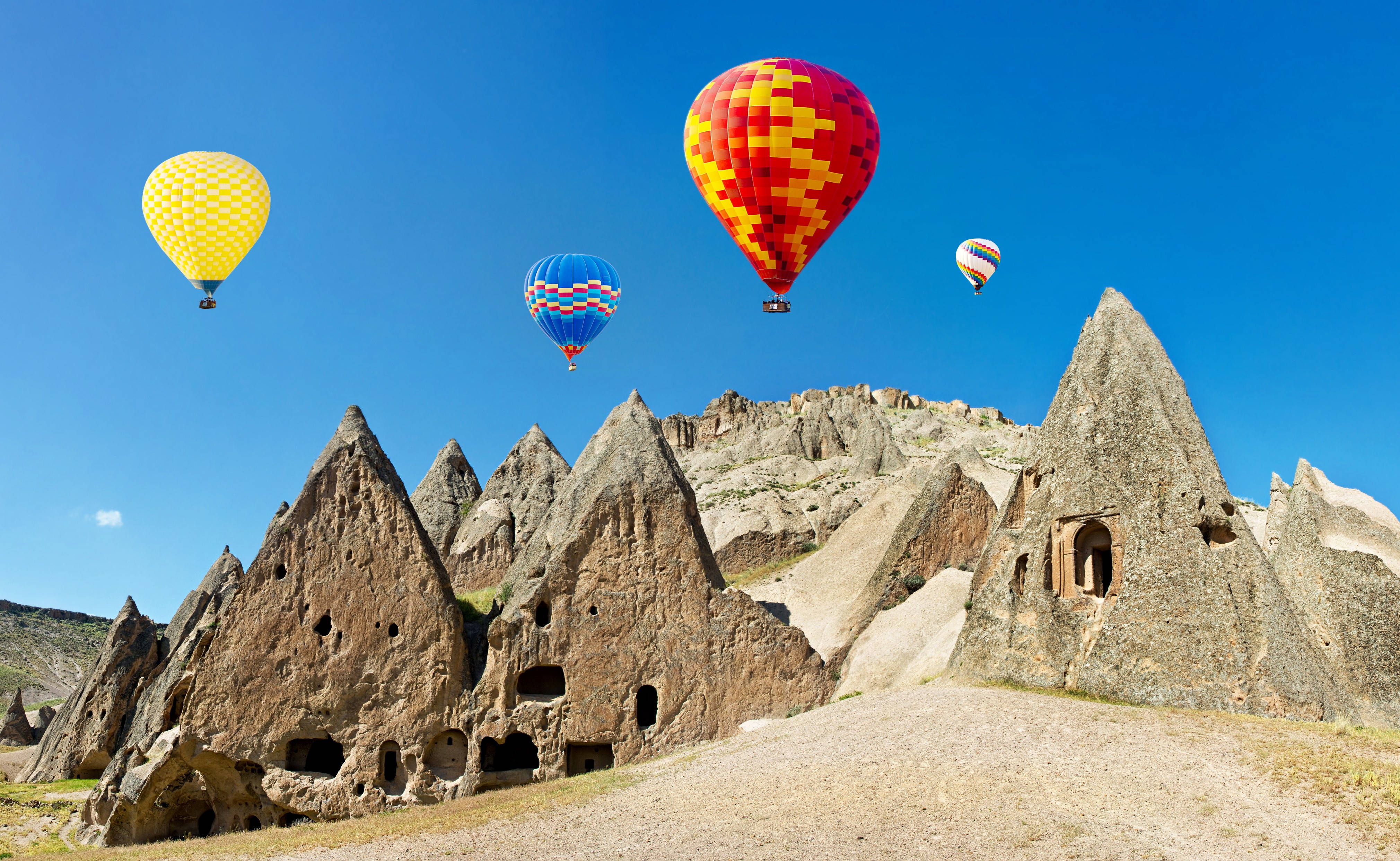 Cappadocia 桌布 壁紙 — 色彩繽紛的熱氣球在蔚藍天空下飄過帶有洞穴住所的古老岩層。
