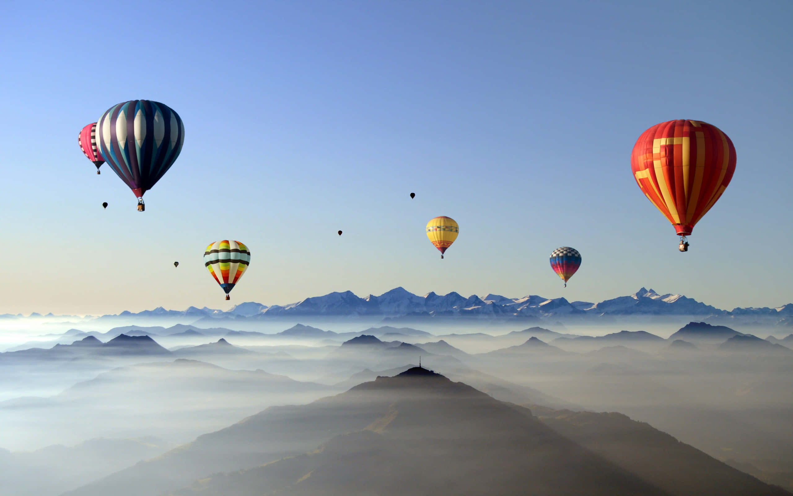 Hot Air Balloon 桌布 壁紙 — 色彩繽紛的熱氣球在雲海上飄浮，遠處是白雪覆蓋的山峰，天空清澈湛藍。