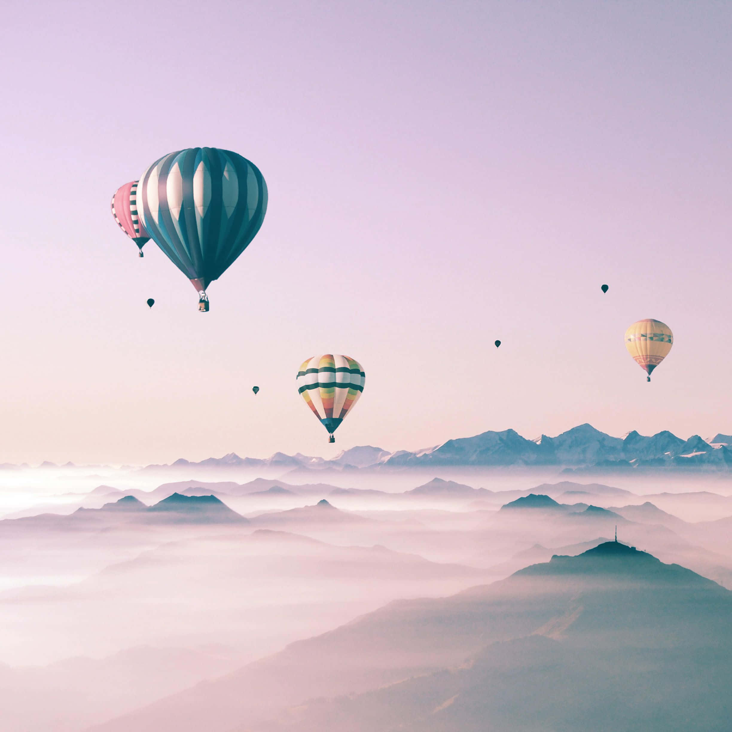 Hot Air Balloon 桌布 壁紙 — 色彩繽紛的熱氣球在霧海上空飄浮，遠處是白雪覆蓋的山峰，天空呈現柔和的粉紅色。