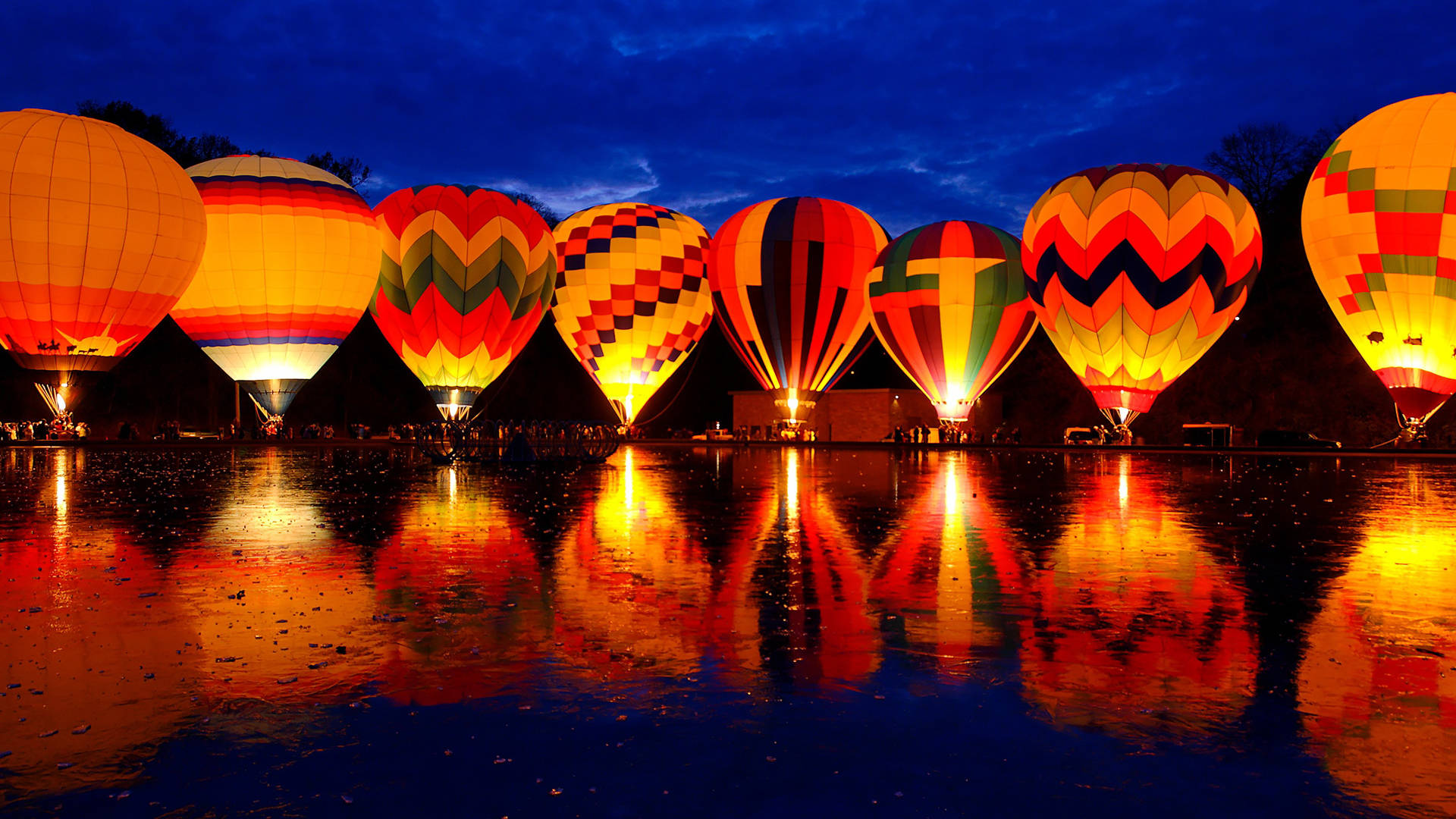 Canberra 桌布 壁紙 — 色彩繽紛的熱氣球在黃昏時發光，其彩色圖案映照在潮濕的反光表面上。