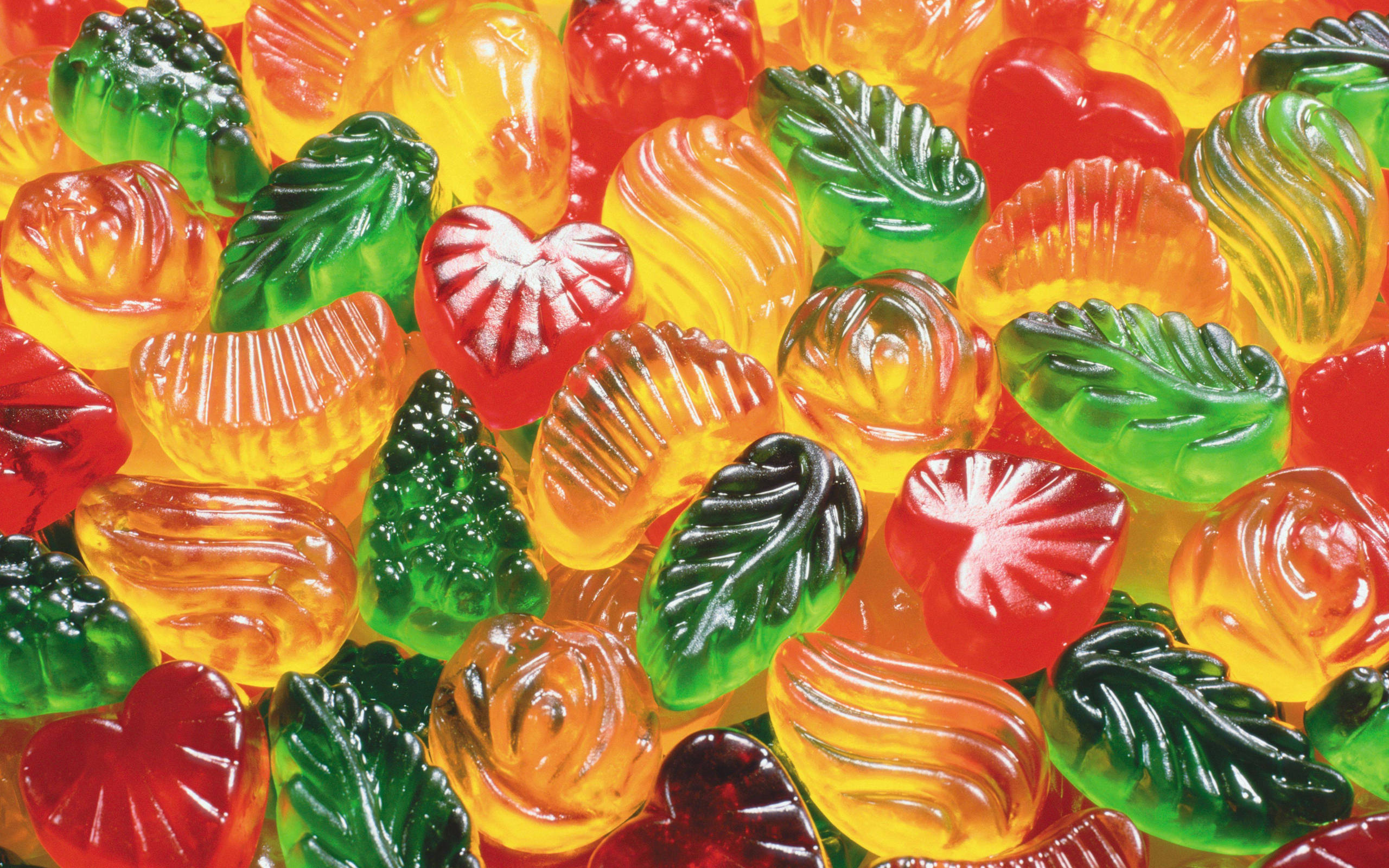 糖果 桌布 壁紙 — 色彩繽紛的特寫鏡頭，展示各種葉子、心形和花朵形狀的軟糖，呈現鮮豔的紅色、橙色和綠色色調。