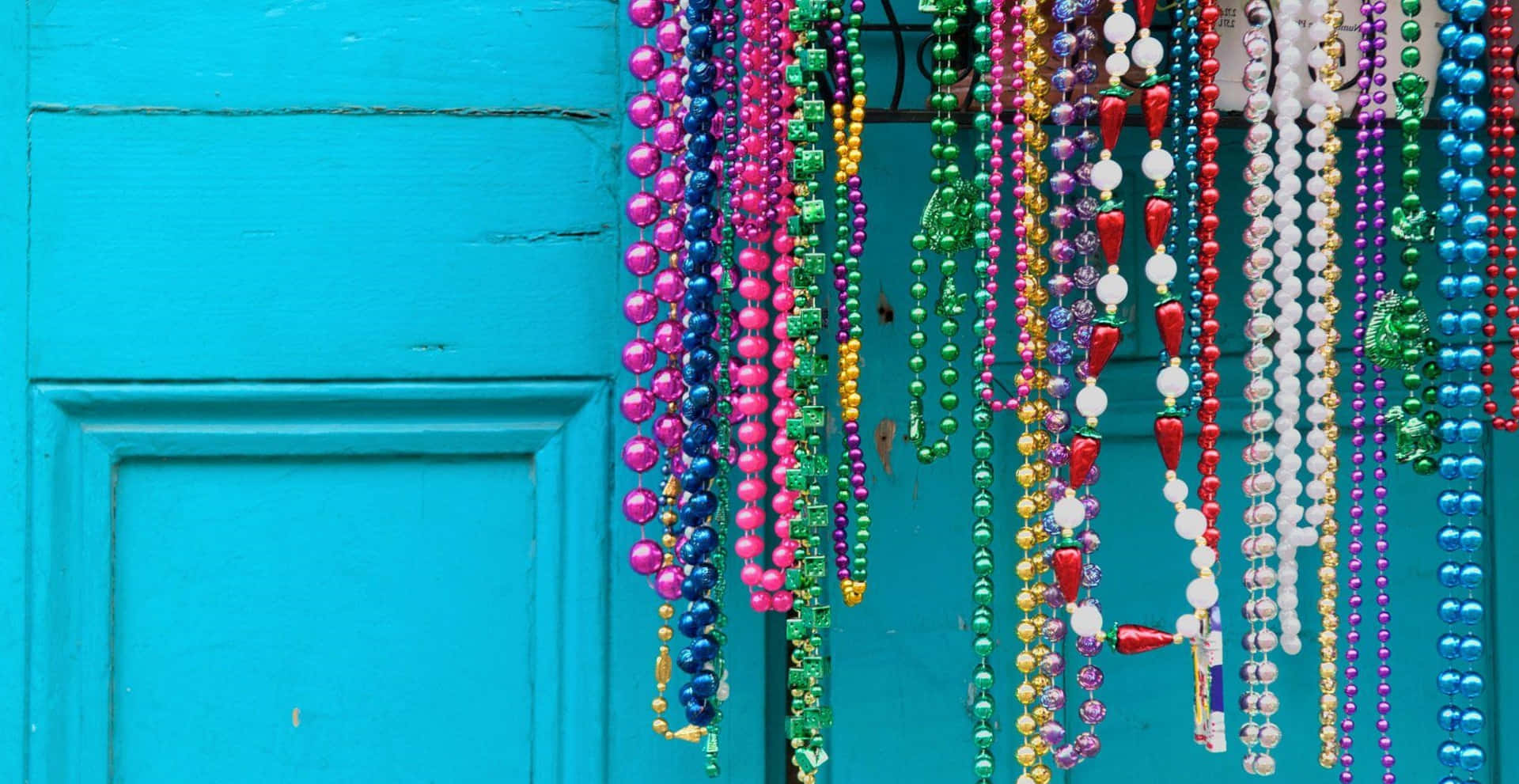 Mardi Gras 桌布 壁紙 — 色彩繽紛的狂歡節珠子以彩虹色調層疊在風化的青綠色木門上。